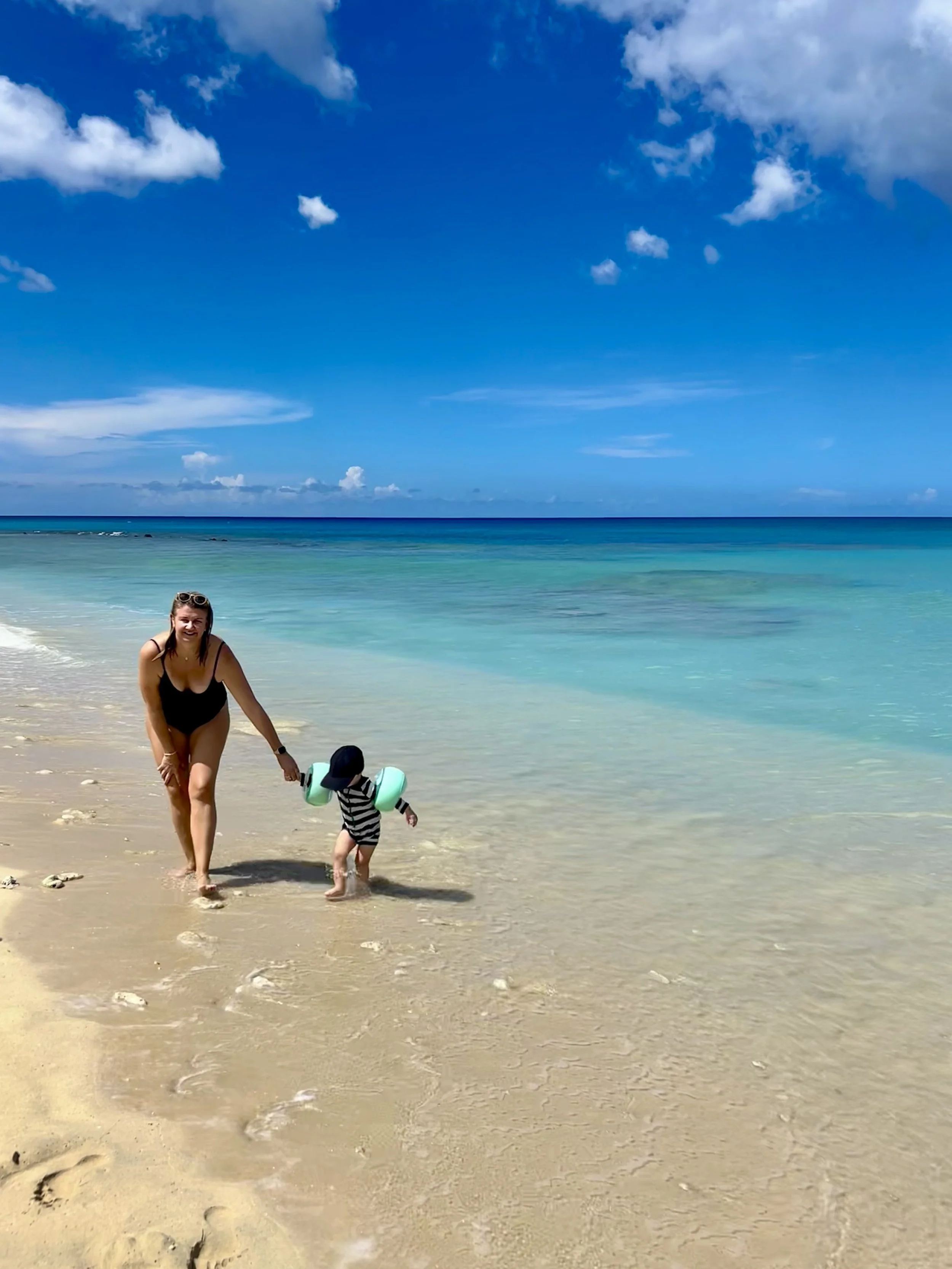 Calm turquoise shallows at Holetown Beach on the west coast of Barbados, with a woman walking a toddler through the water