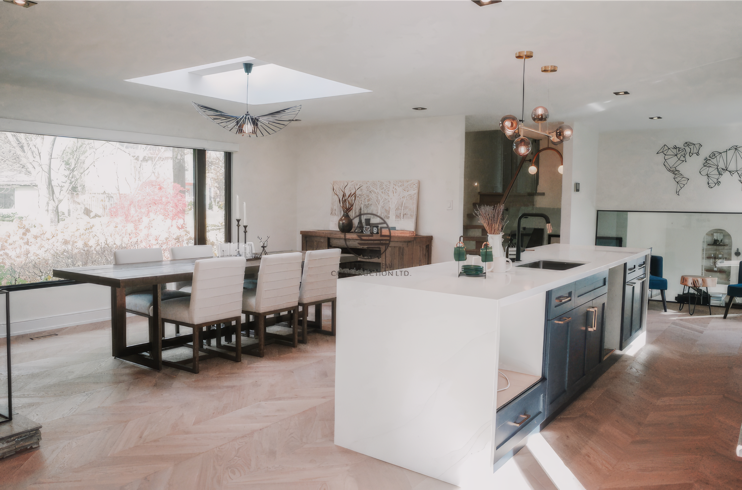 Modern open concept kitchen and dining renovation with large island, skylight ceiling, and herringbone wood flooring in a Toronto home.