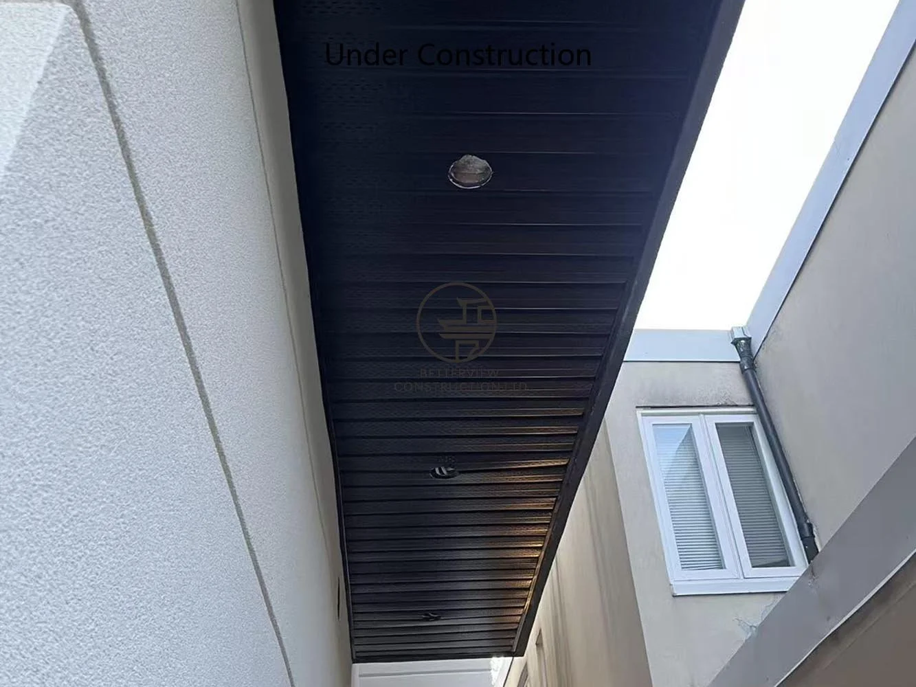 Modern soffit with wood-look panels and recessed lighting, complementing the contemporary stucco exterior of the rear addition.