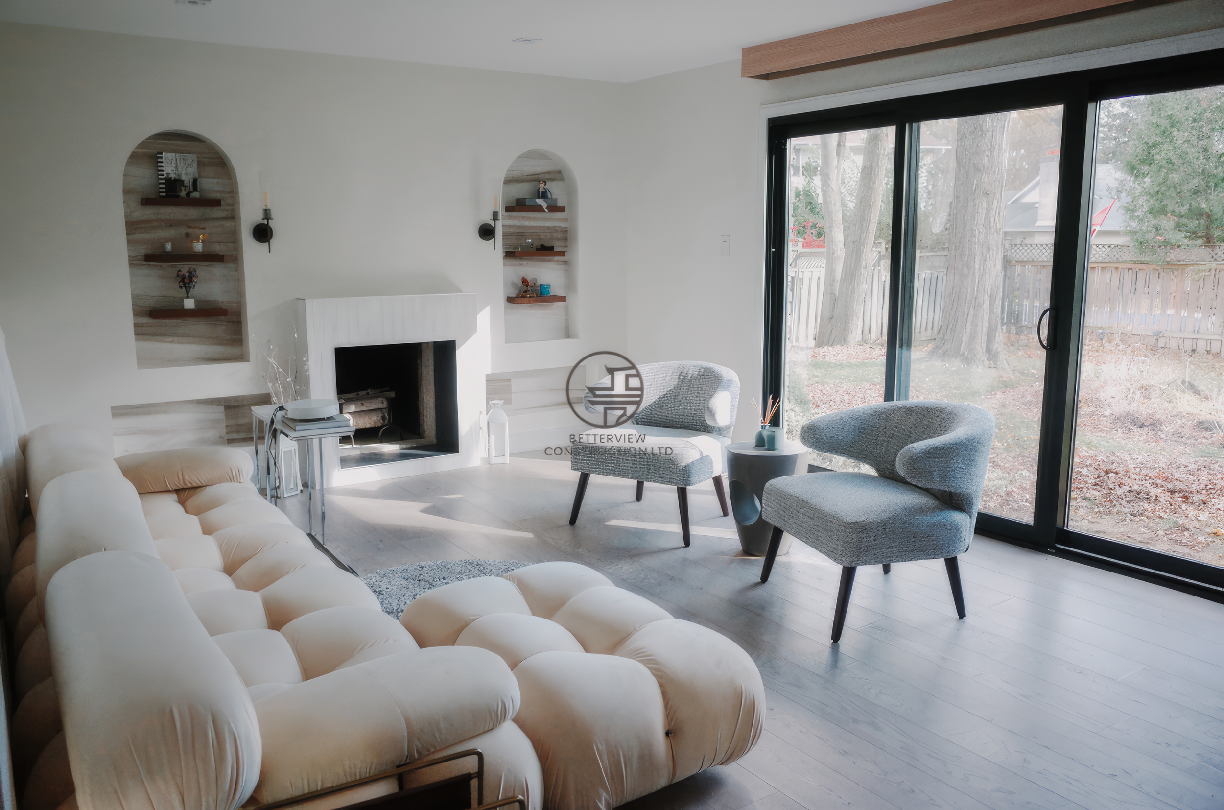 Modern living room renovation with fireplace feature wall, built-in shelving niches, and large sliding glass doors in a Toronto home.