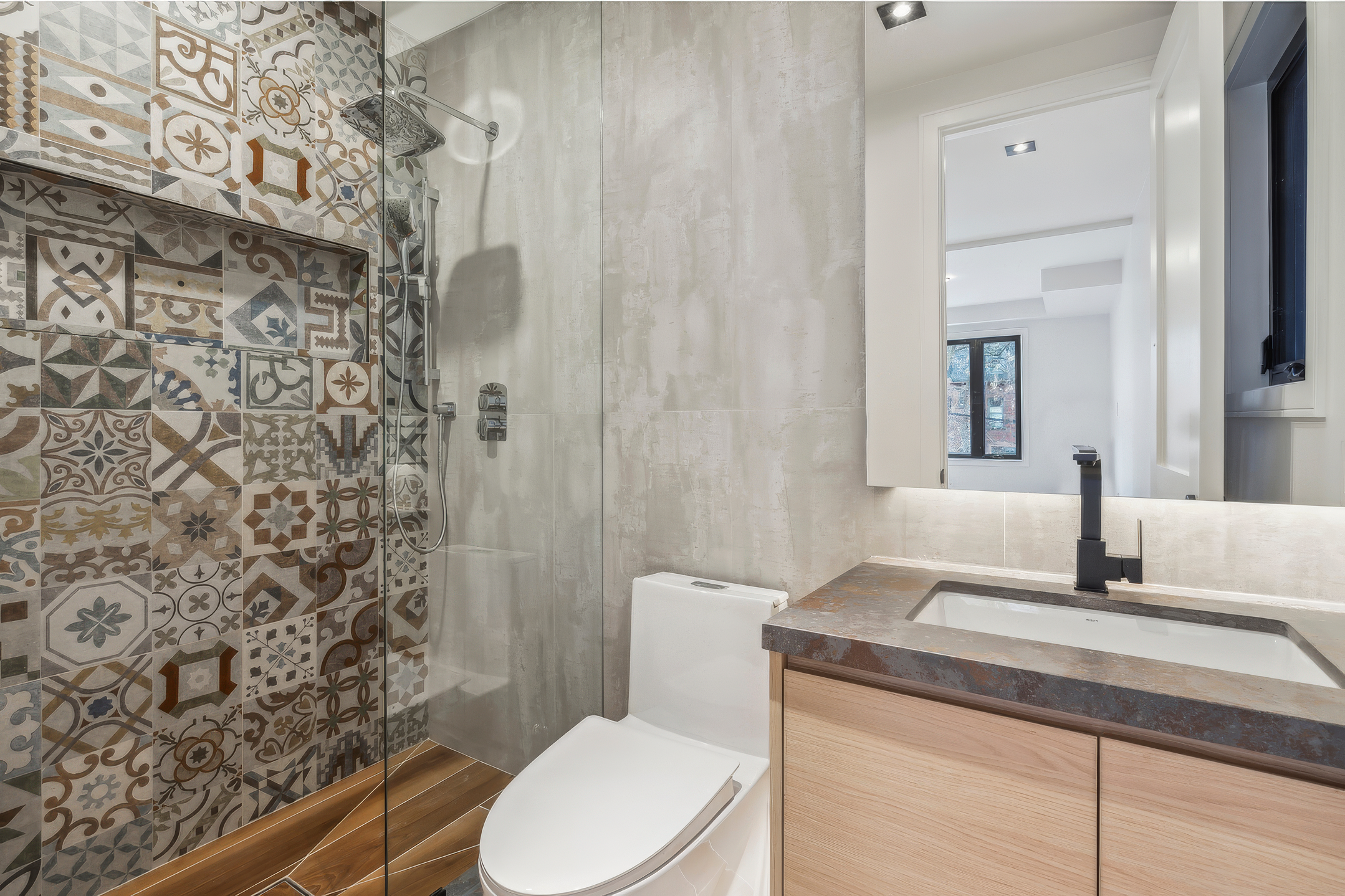 Modern bathroom with patterned tile shower wall, glass enclosure, floating vanity, and matte black fixtures in a residential home renovation project