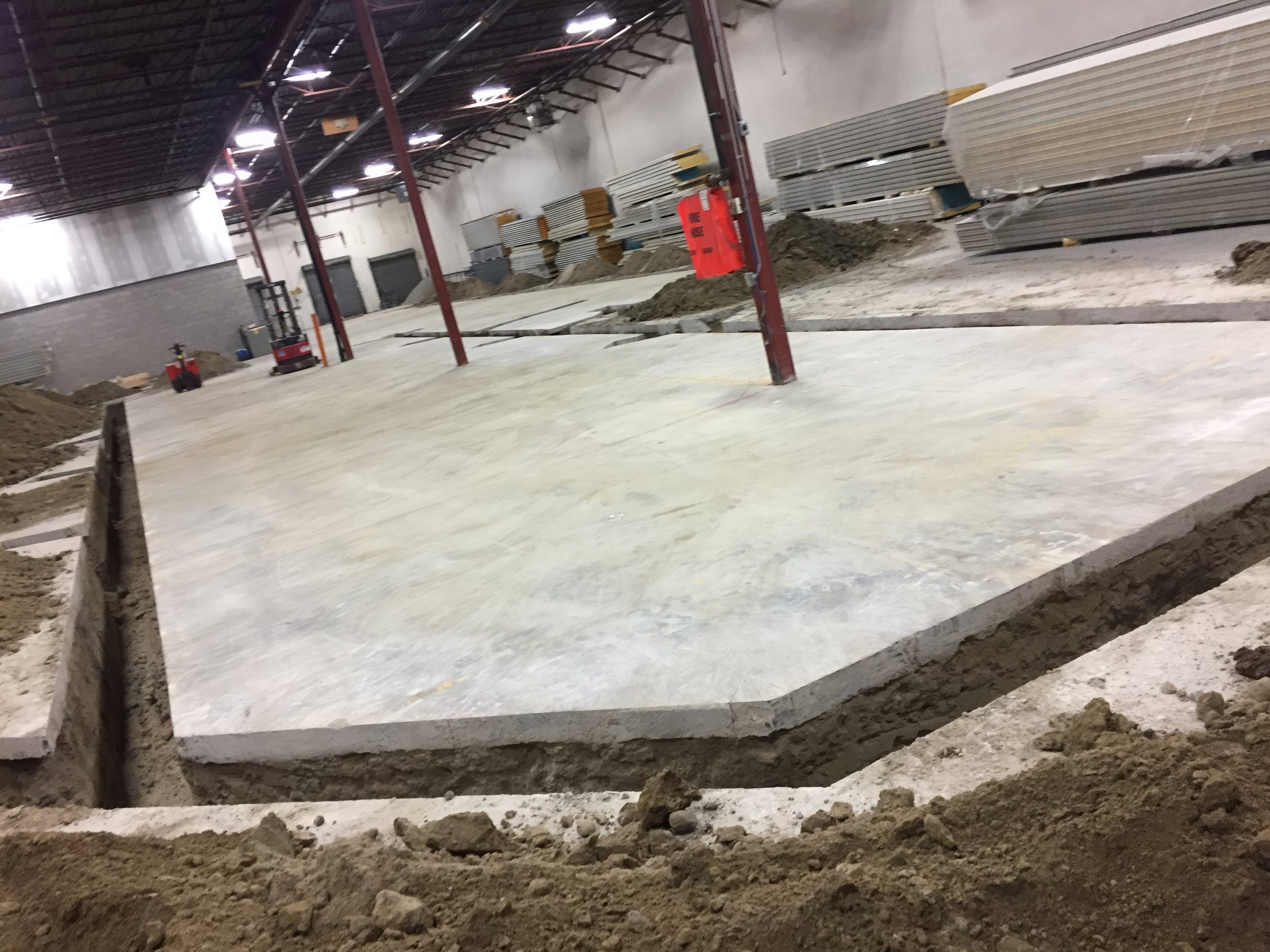 Commercial warehouse renovation showing newly installed concrete slab alongside ongoing trench excavation for structural and plumbing upgrades in Toronto