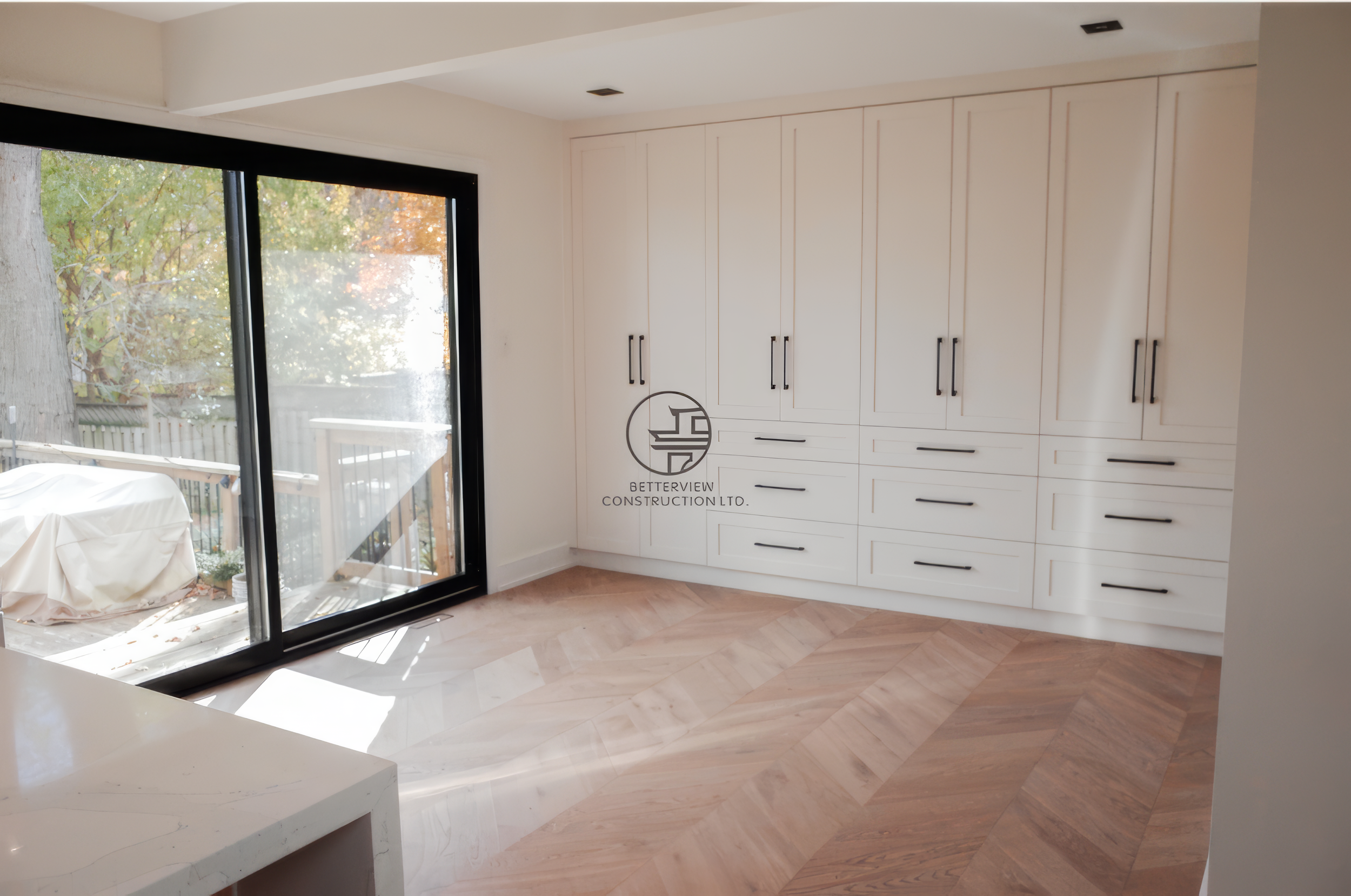 Modern kitchen renovation with floor-to-ceiling white cabinetry, herringbone wood flooring, and large sliding glass doors in a Toronto home.