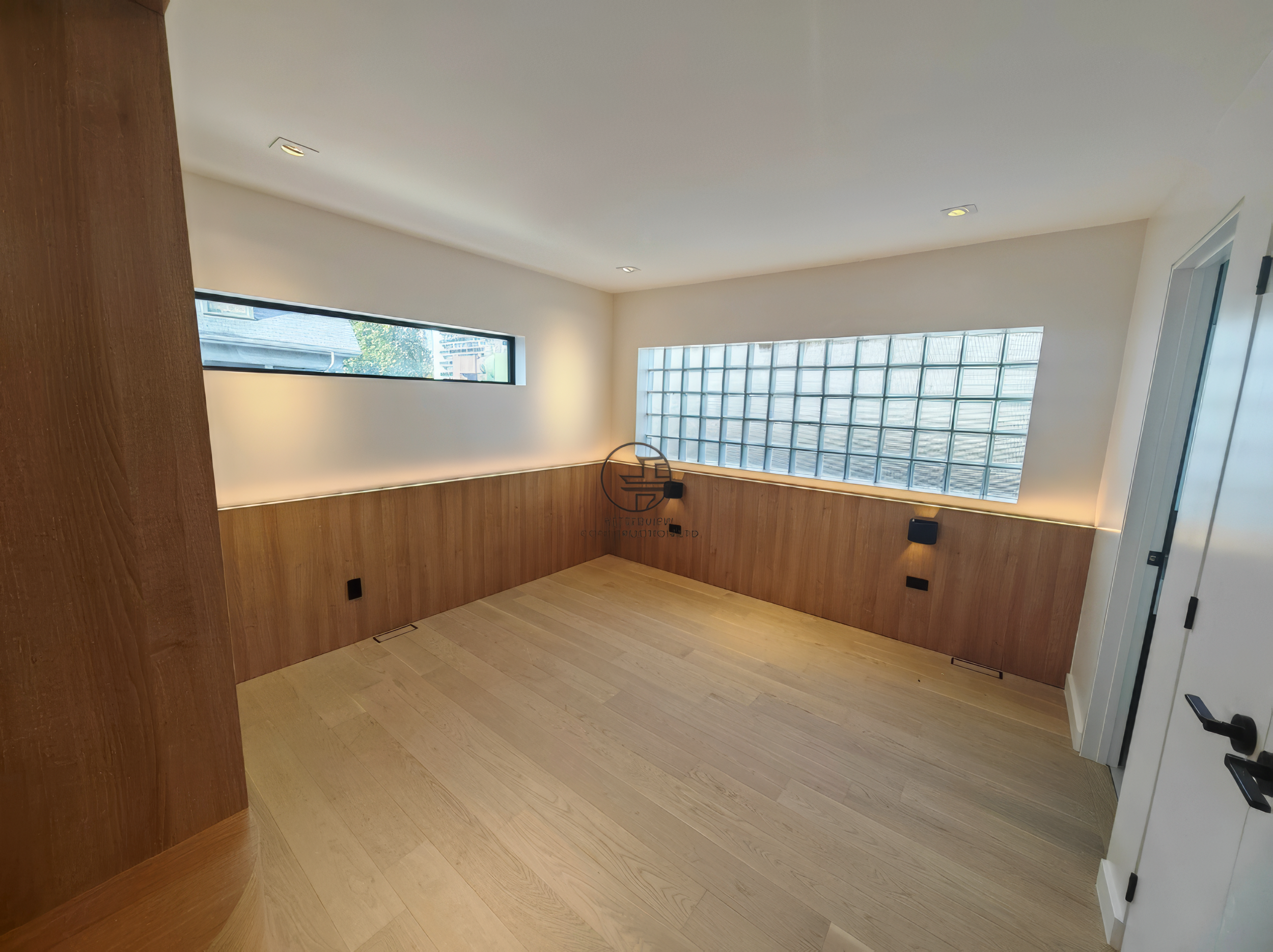 modern basement renovation room with wood panel walls, glass block window, and light hardwood flooring