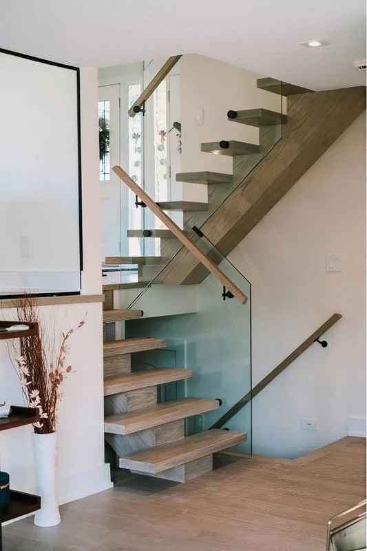 Modern wooden staircase with glass railing and exposed black hardware in a contemporary home interior.