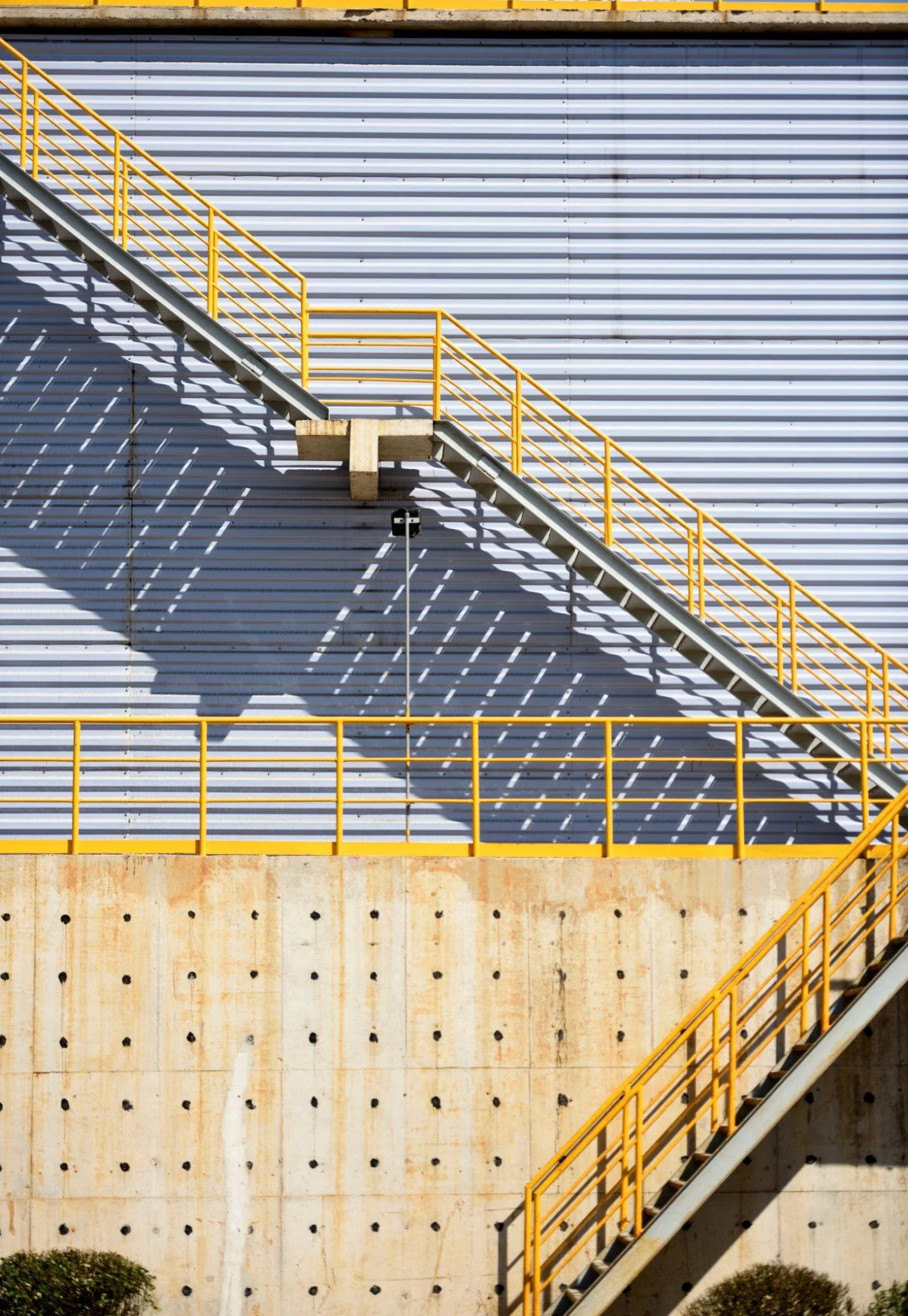 Exterior industrial metal staircase with yellow safety railings on factory building wall
