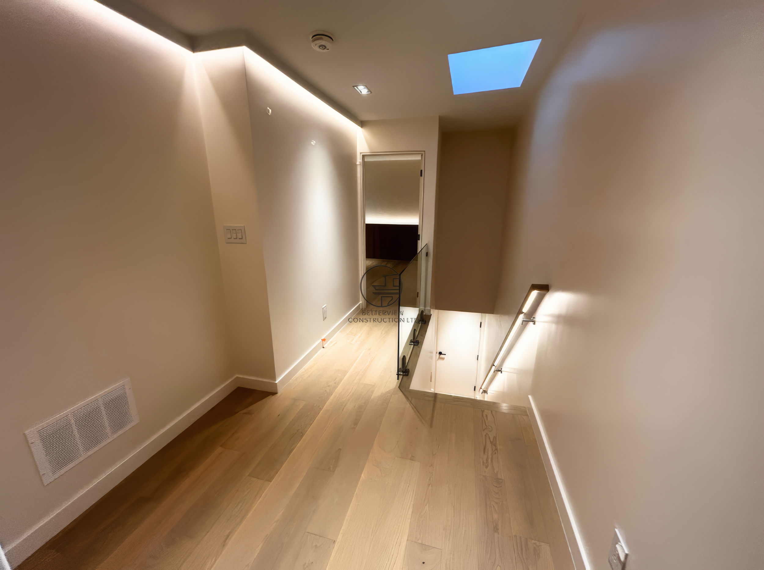 modern hallway with skylight, glass stair railing, and light hardwood flooring in residential renovation