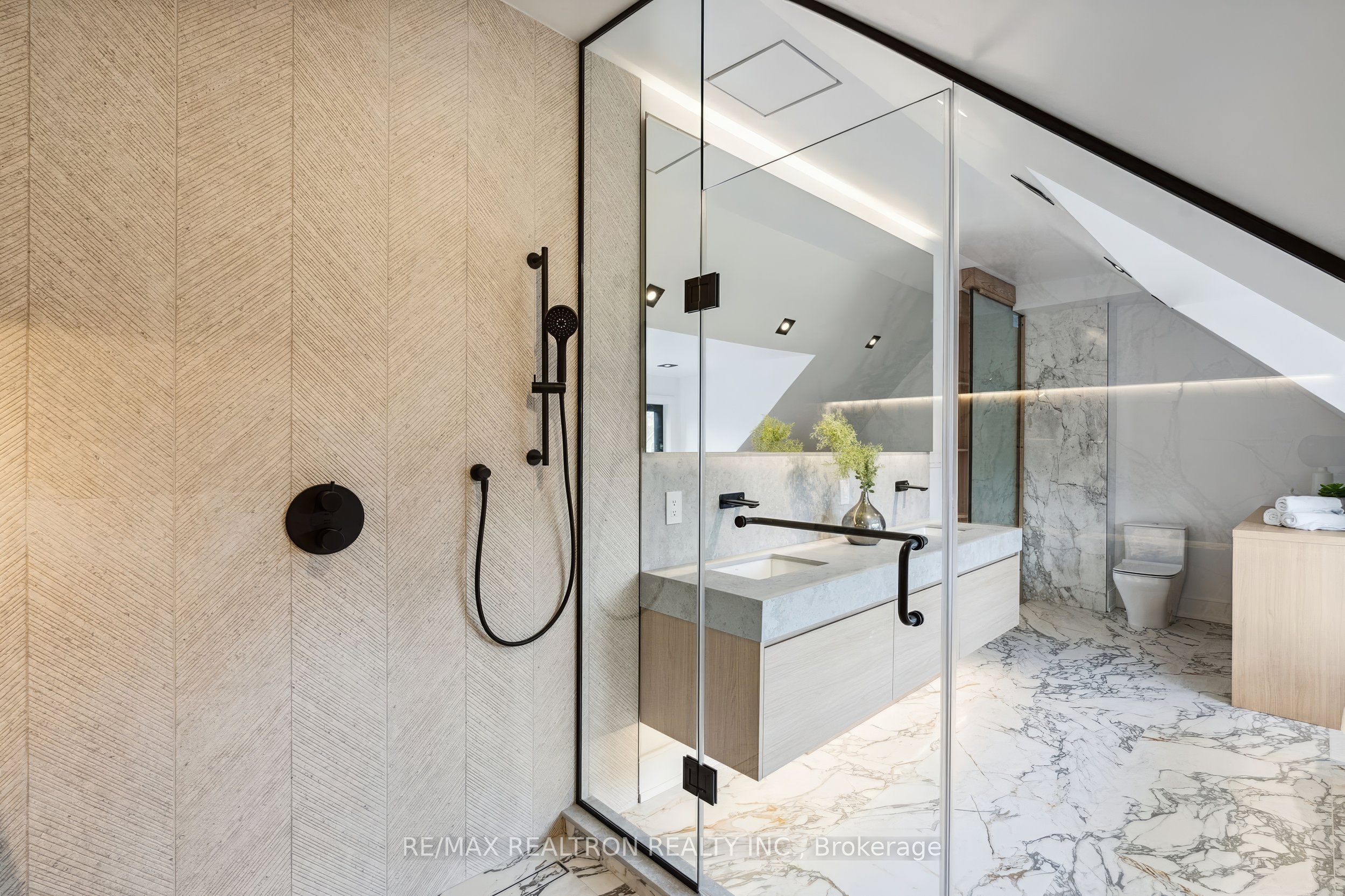 Modern bathroom renovation with marble flooring, glass walk-in shower, skylight ceiling, and minimalist vanity design.