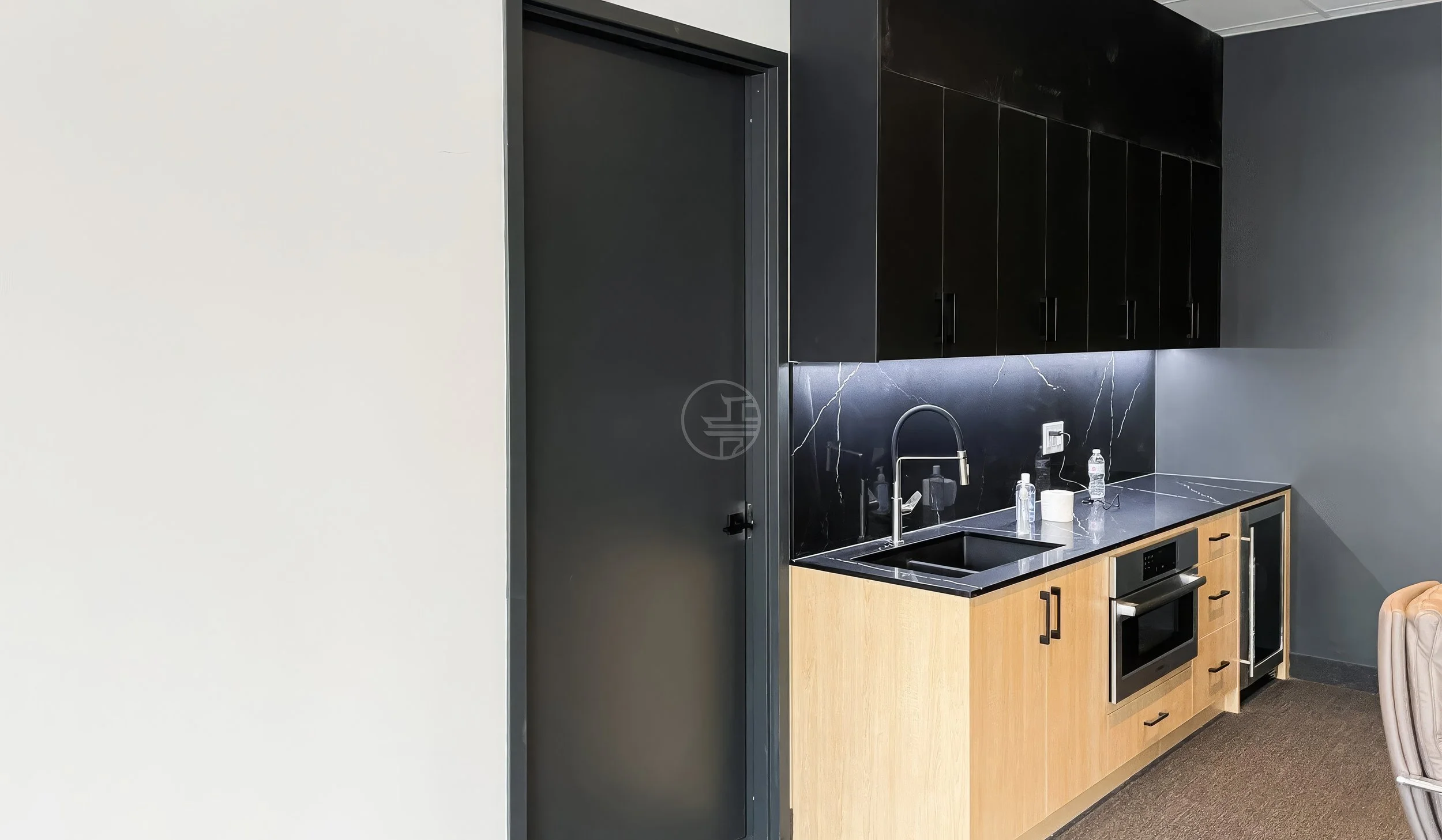 Modern office kitchenette renovation in Toronto featuring black cabinetry, stone backsplash, built-in appliances, and contemporary workspace design