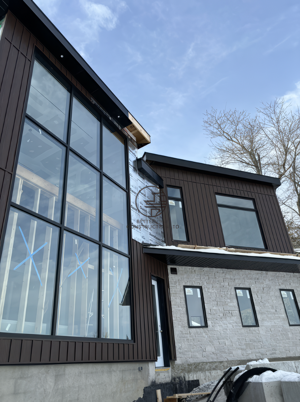 Modern home exterior with large floor to ceiling windows, wood siding and stone facade under construction