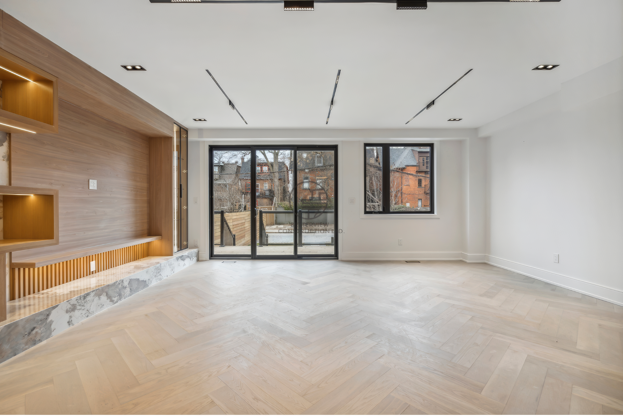 Modern living room with herringbone wood flooring, large sliding doors, built-in feature wall with wood paneling, and recessed ceiling lighting.