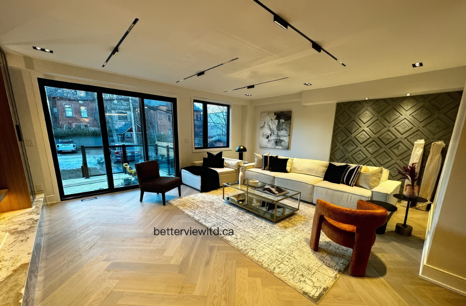Spacious modern living room with large windows, herringbone wood flooring, feature wall, recessed lighting, and contemporary furniture layout.