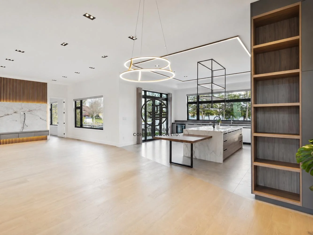 Modern open-concept living and kitchen area with feature wall, custom shelving, LED lighting, light wood flooring, and spacious minimalist interior design.