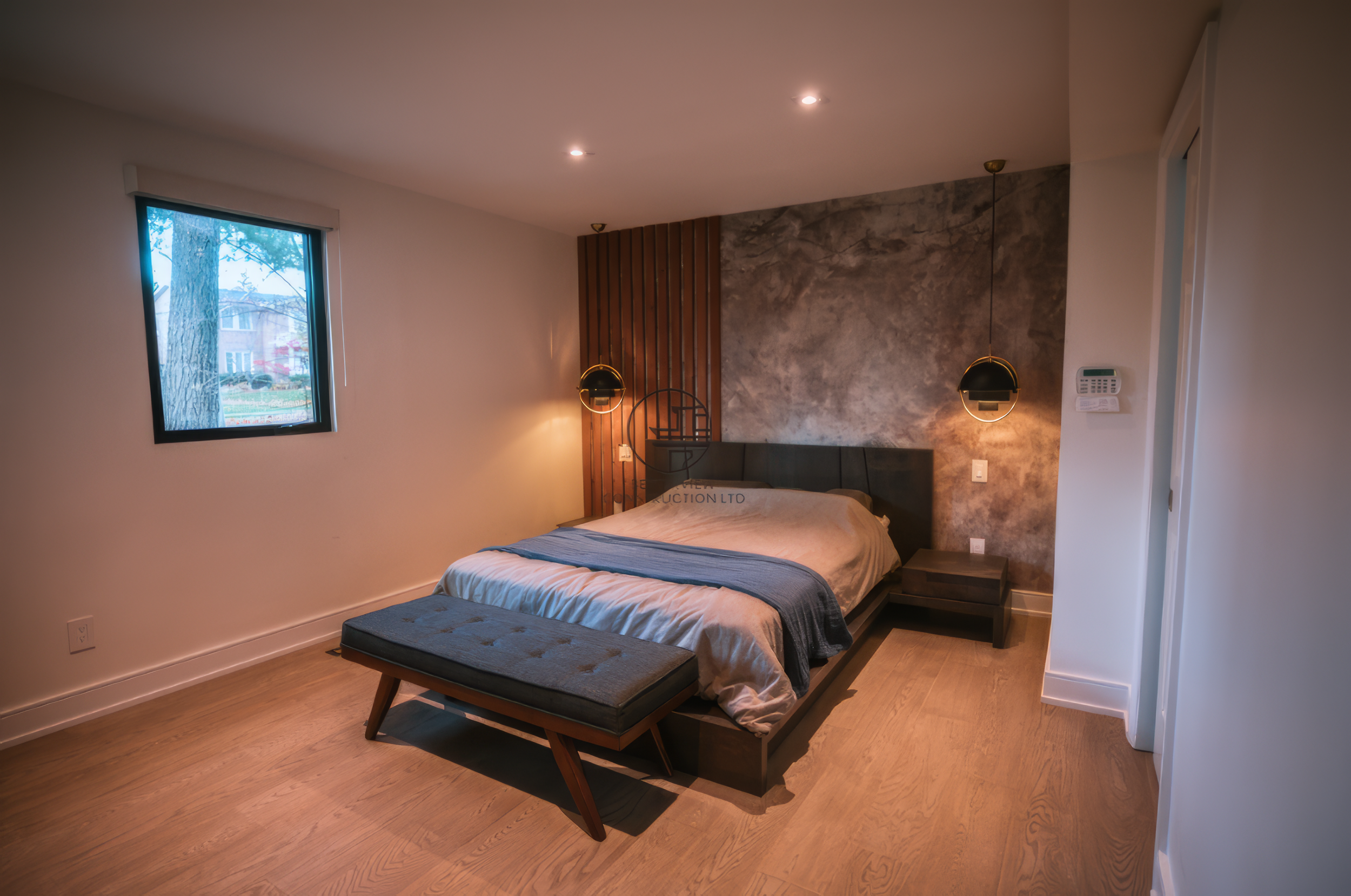 Modern bedroom renovation with wood accent wall, upholstered bed, and warm lighting in a Toronto home.