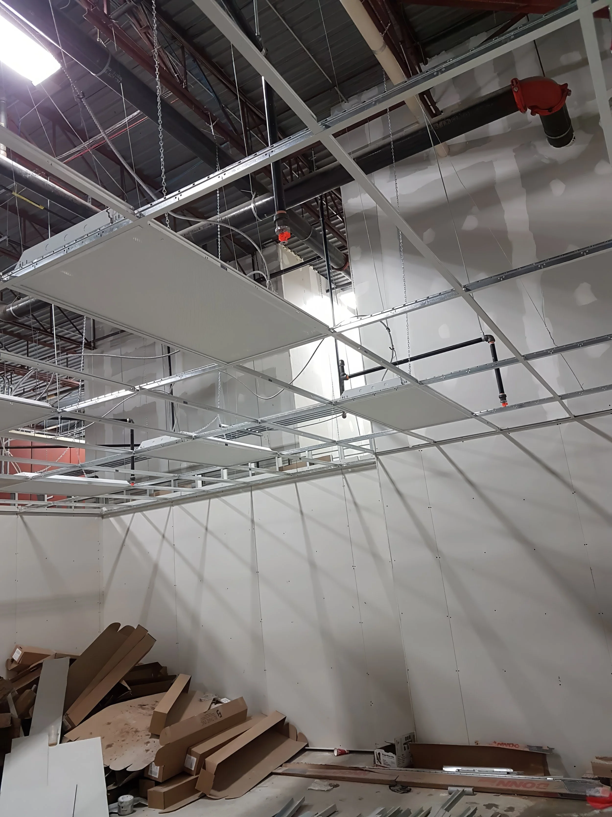 Commercial interior construction showing suspended ceiling grid installation with integrated plumbing, fire sprinkler, and mechanical systems in a warehouse renovation in Toronto