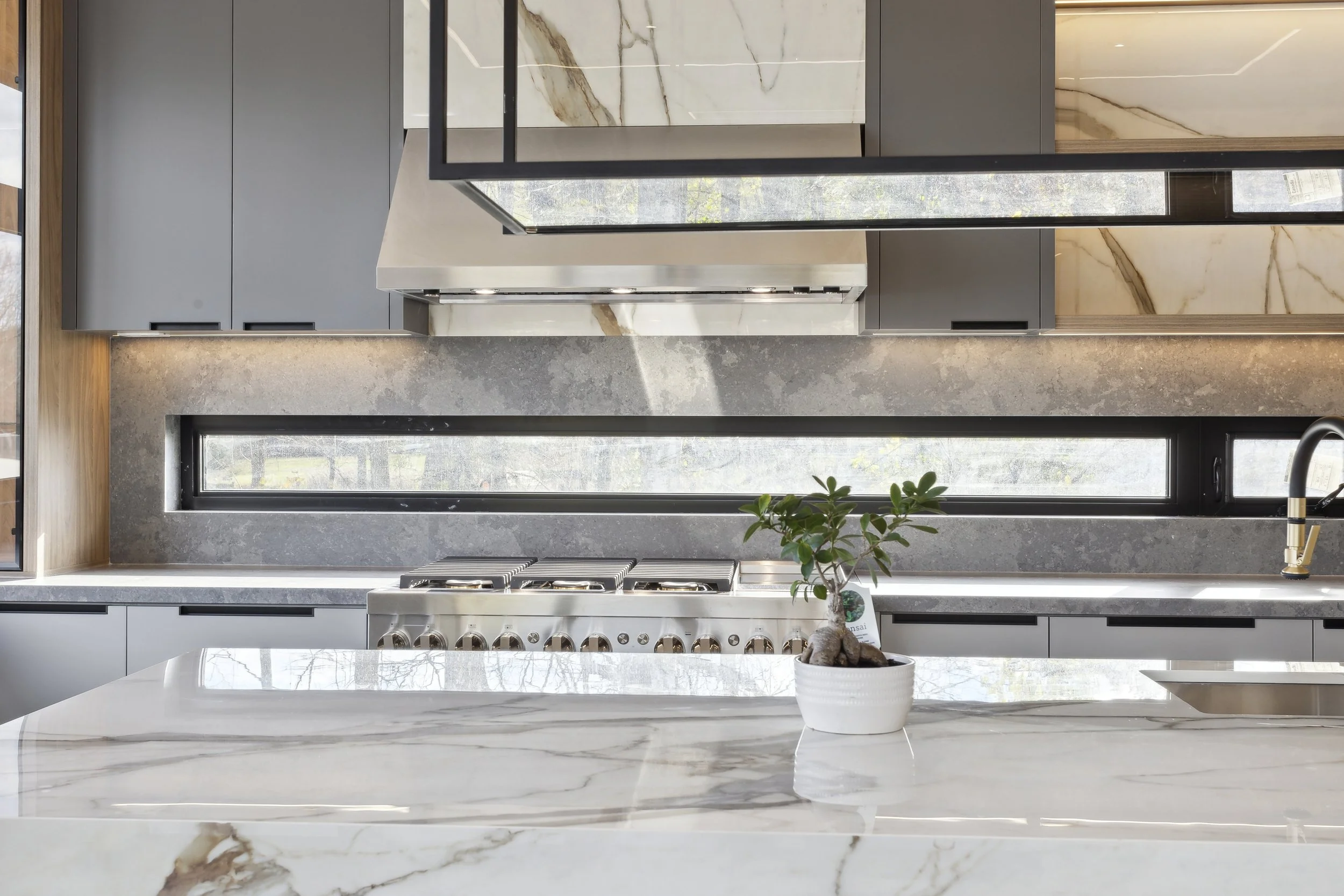 Modern kitchen with gray cabinets, marble backsplash, and a white countertop featuring a potted plant and a built-in stovetop.