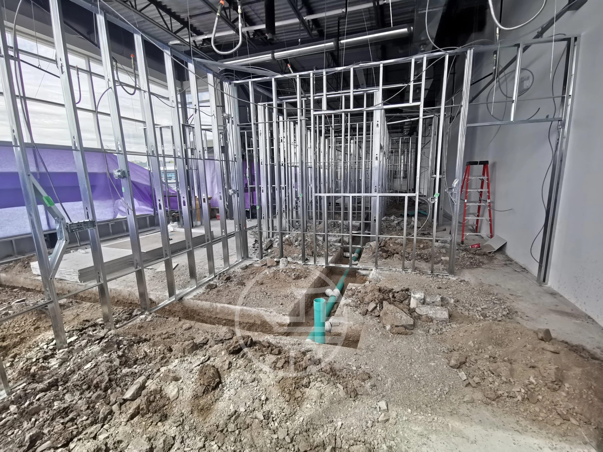Commercial renovation site with underground plumbing installation, trenching, and steel framing structure during interior construction