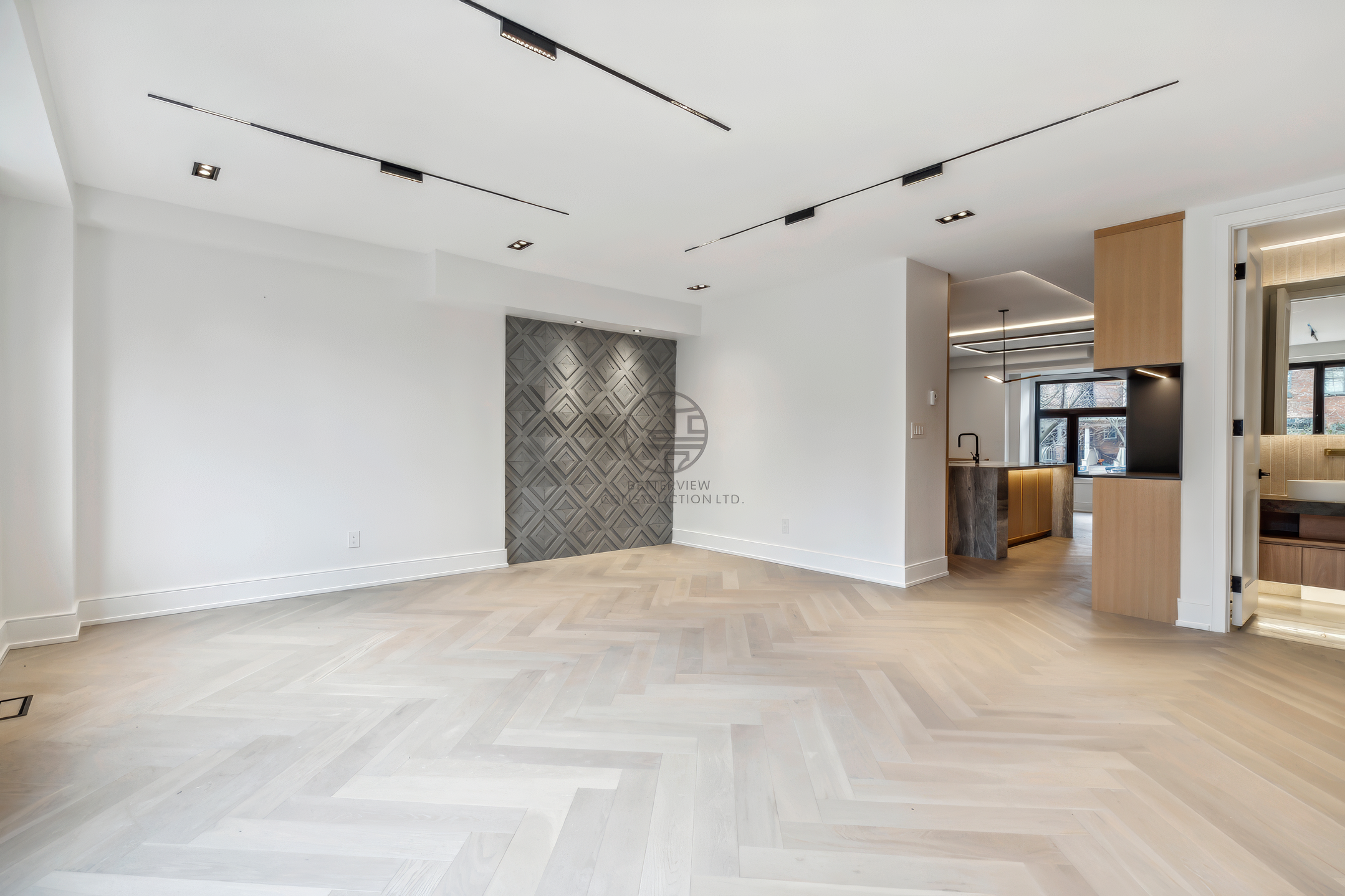 Spacious modern living area with herringbone wood flooring, feature wall, recessed lighting, and open layout connecting to kitchen in a luxury home renovation project