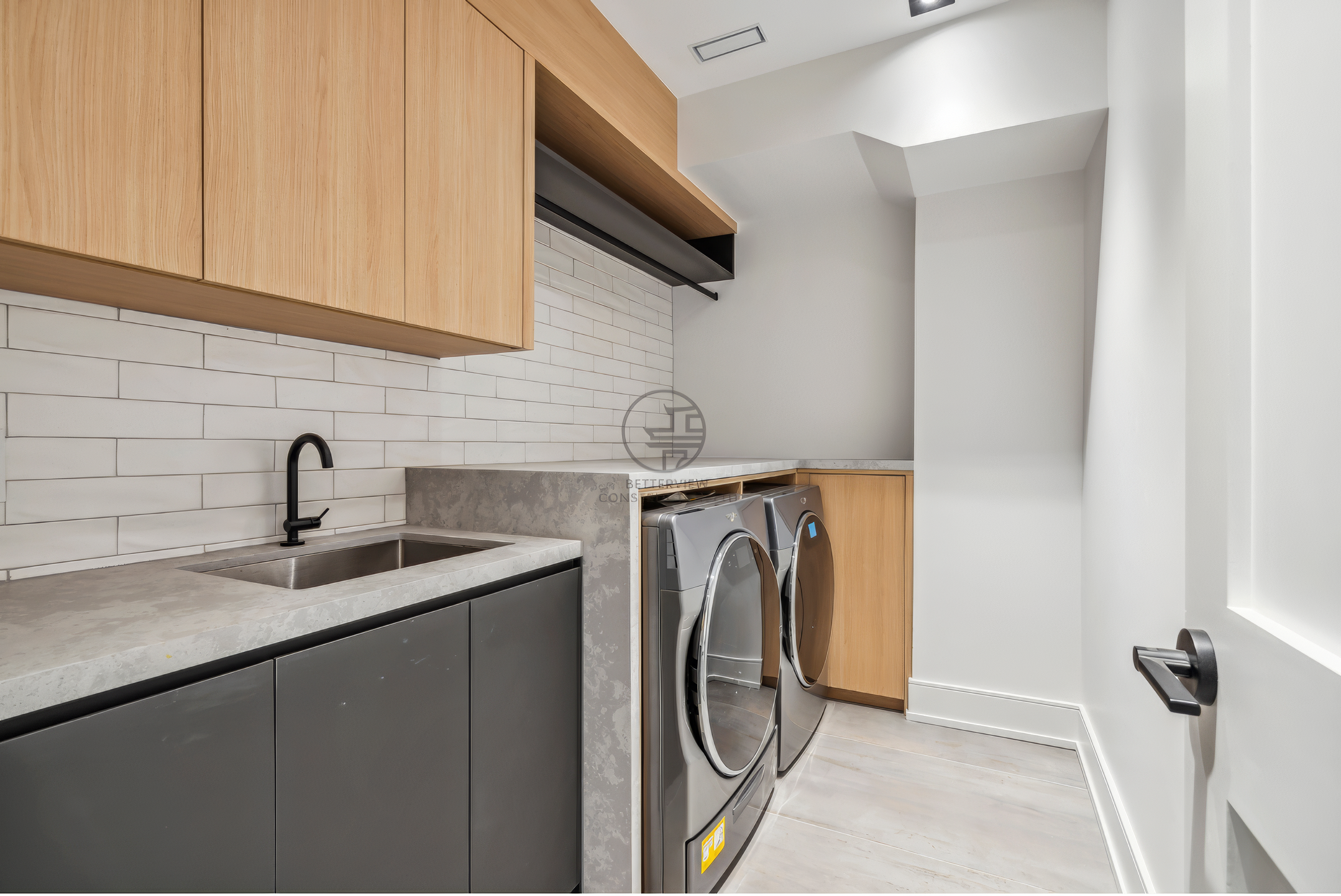 Modern laundry room with front-load washer and dryer, wood cabinetry, utility sink, white tile backsplash, and minimalist design.