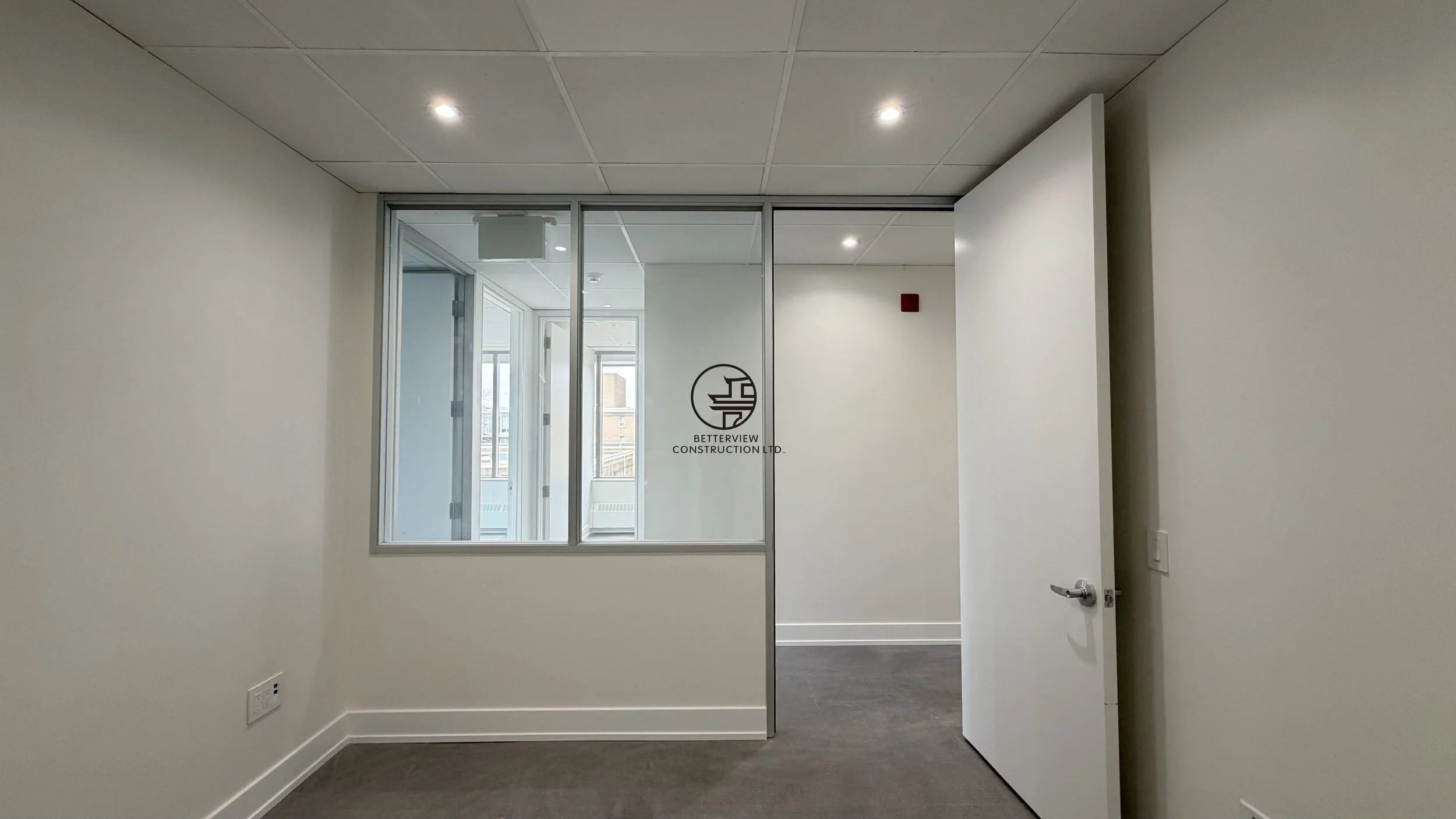 Private office room with interior window, open door, and recessed lighting in commercial renovation
