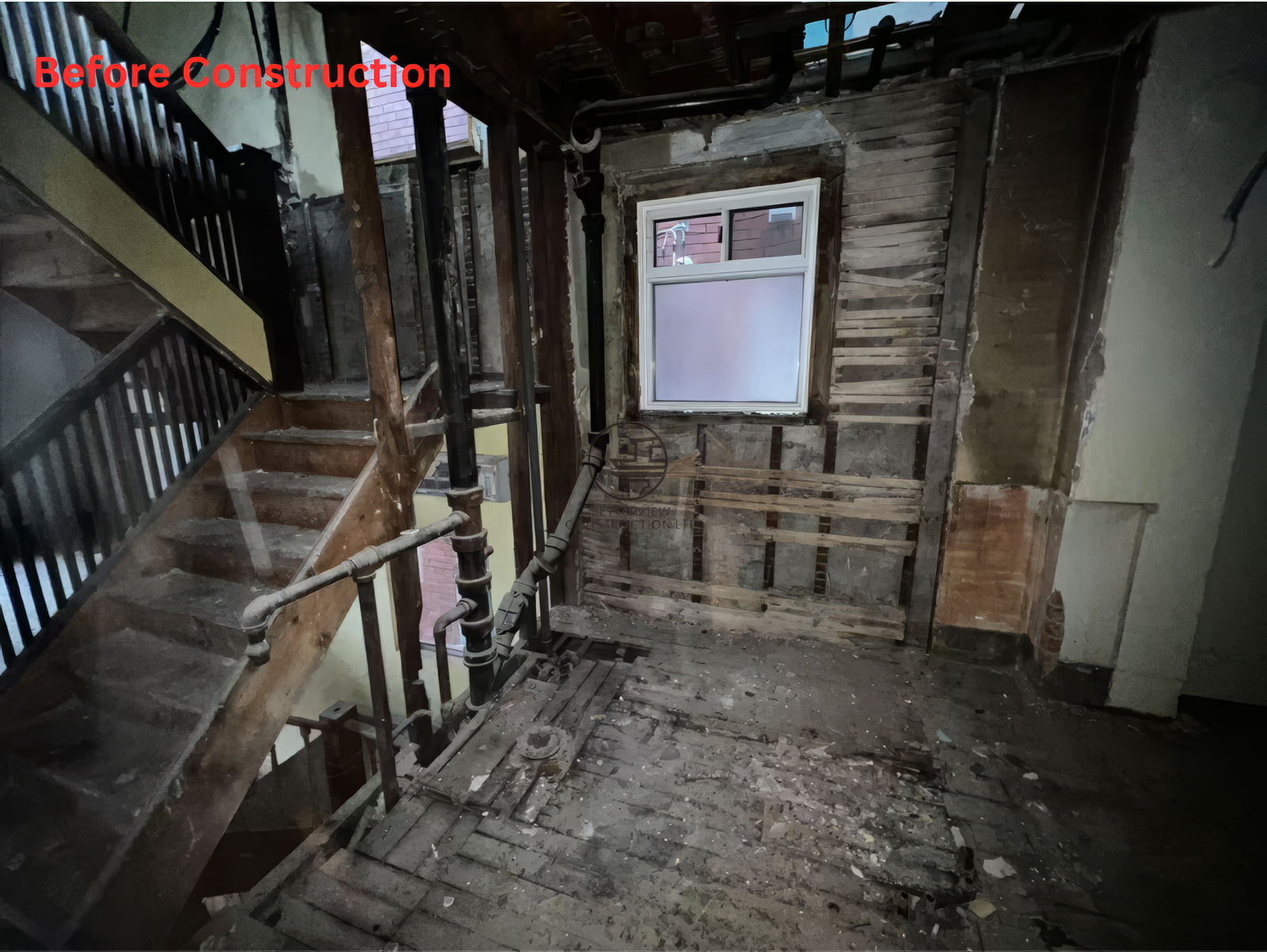Before construction interior showing stripped walls, exposed framing, old staircase, and damaged flooring in a residential home renovation project
