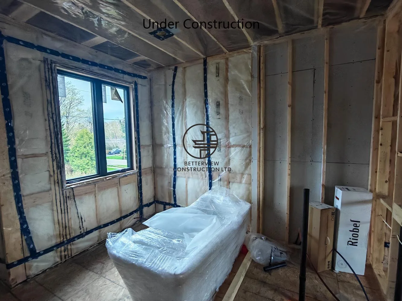 Bathroom under construction with plumbing rough-ins, insulation, and framing during a residential home renovation project.