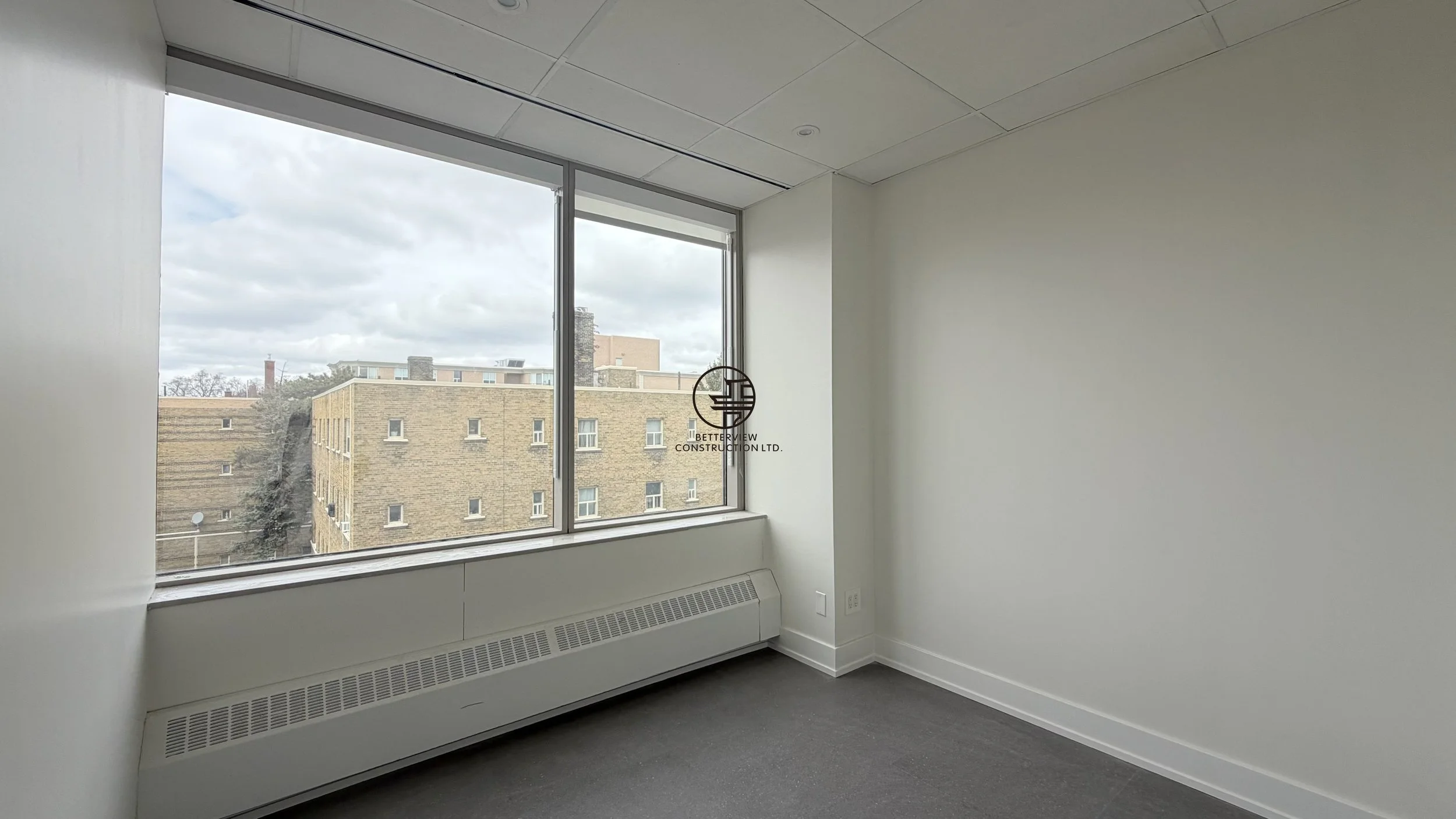 Private office room with large window, carpet flooring, and natural light in commercial renovation