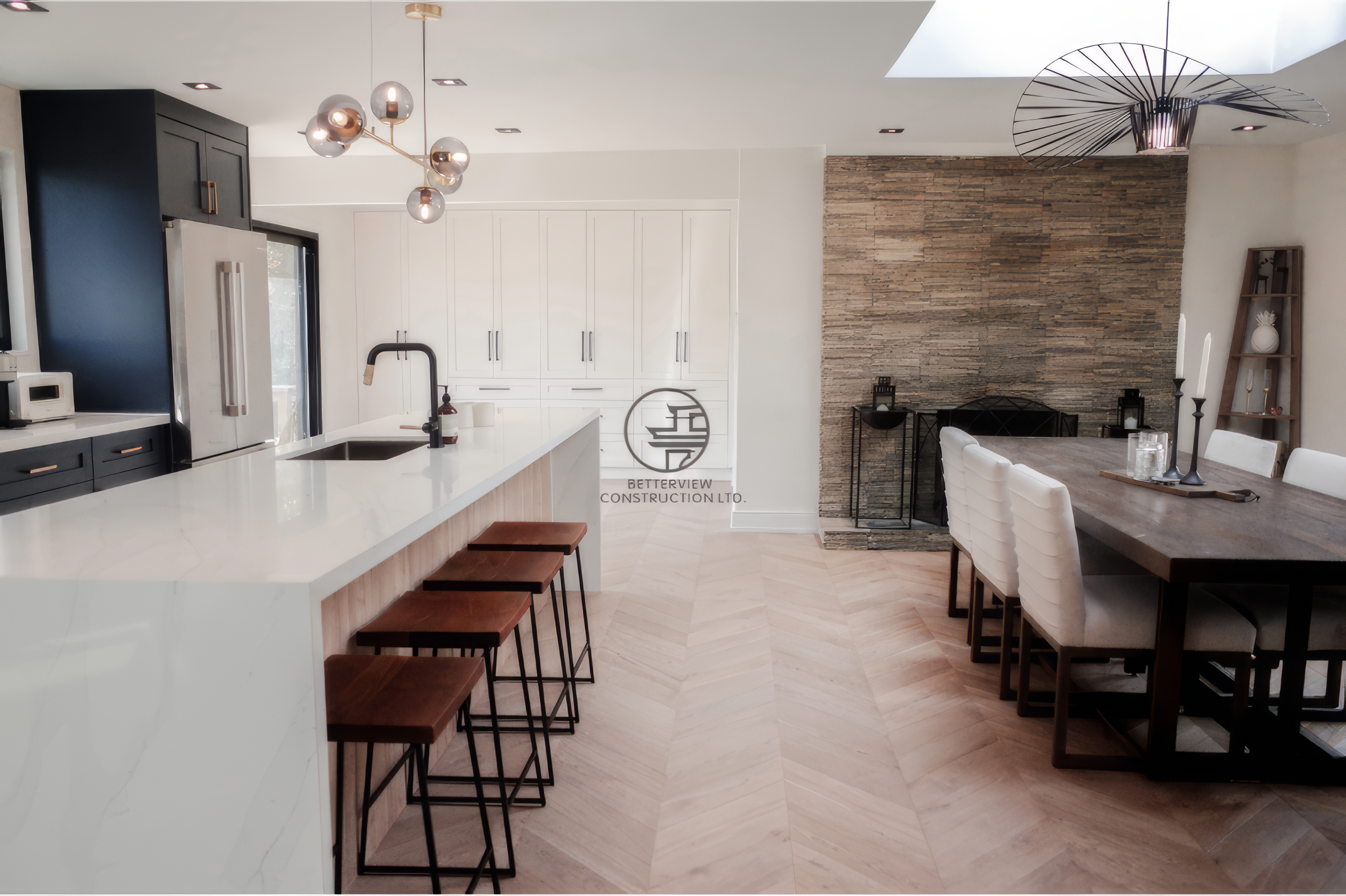 Modern open concept kitchen and dining renovation with large waterfall island, bar stools, skylight ceiling, and stone fireplace wall.