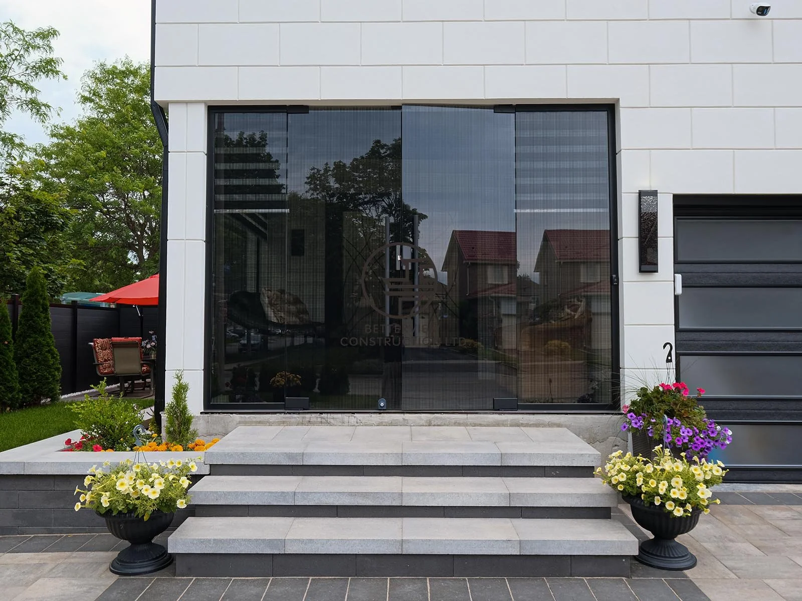 Floor-to-ceiling front windows enhance the entrance with abundant natural light while showcasing the clean lines and contemporary design of the home addition.