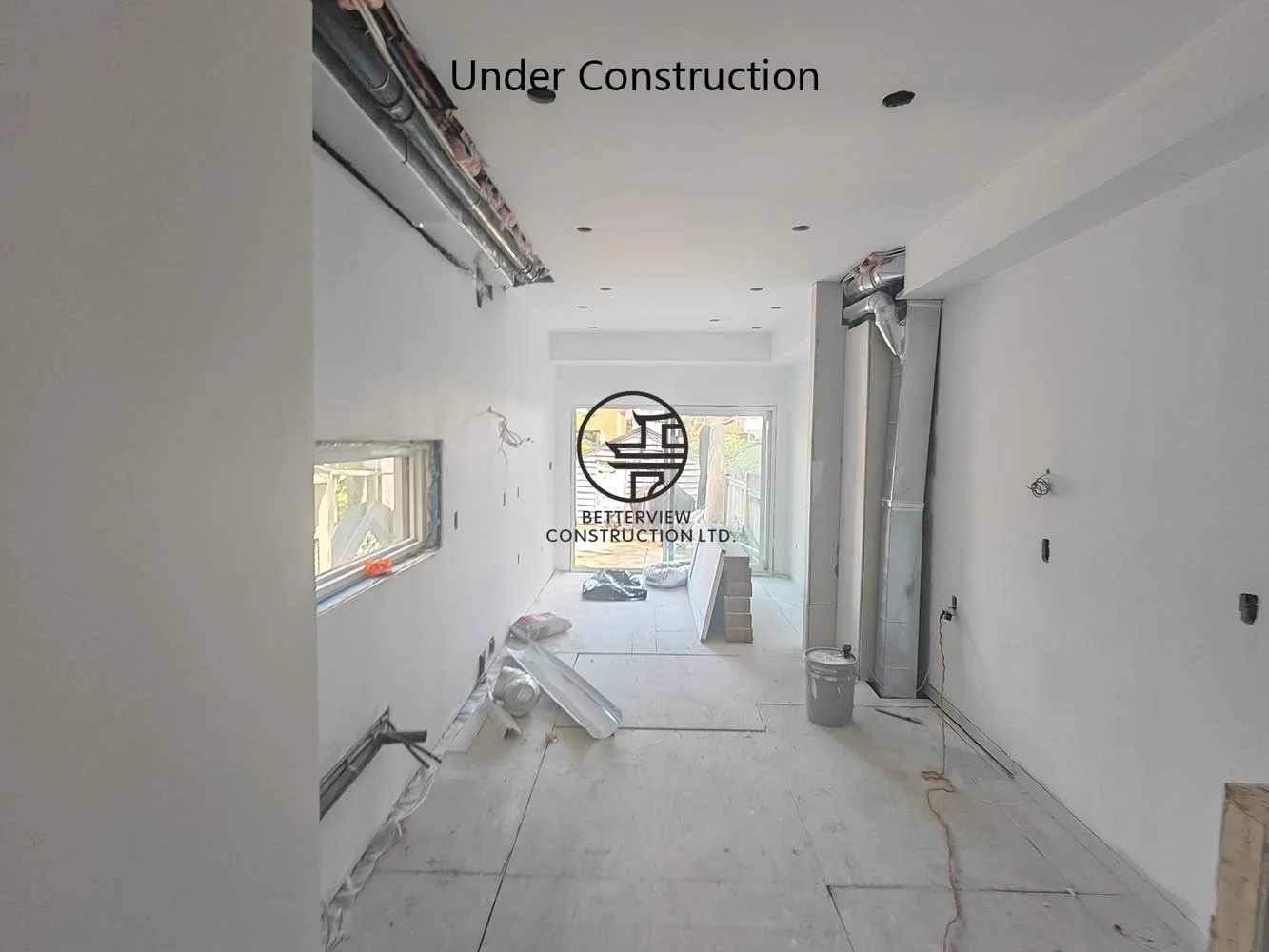 Open concept kitchen under construction featuring drywall installation, custom layout preparation, and large windows overlooking the rear yard.