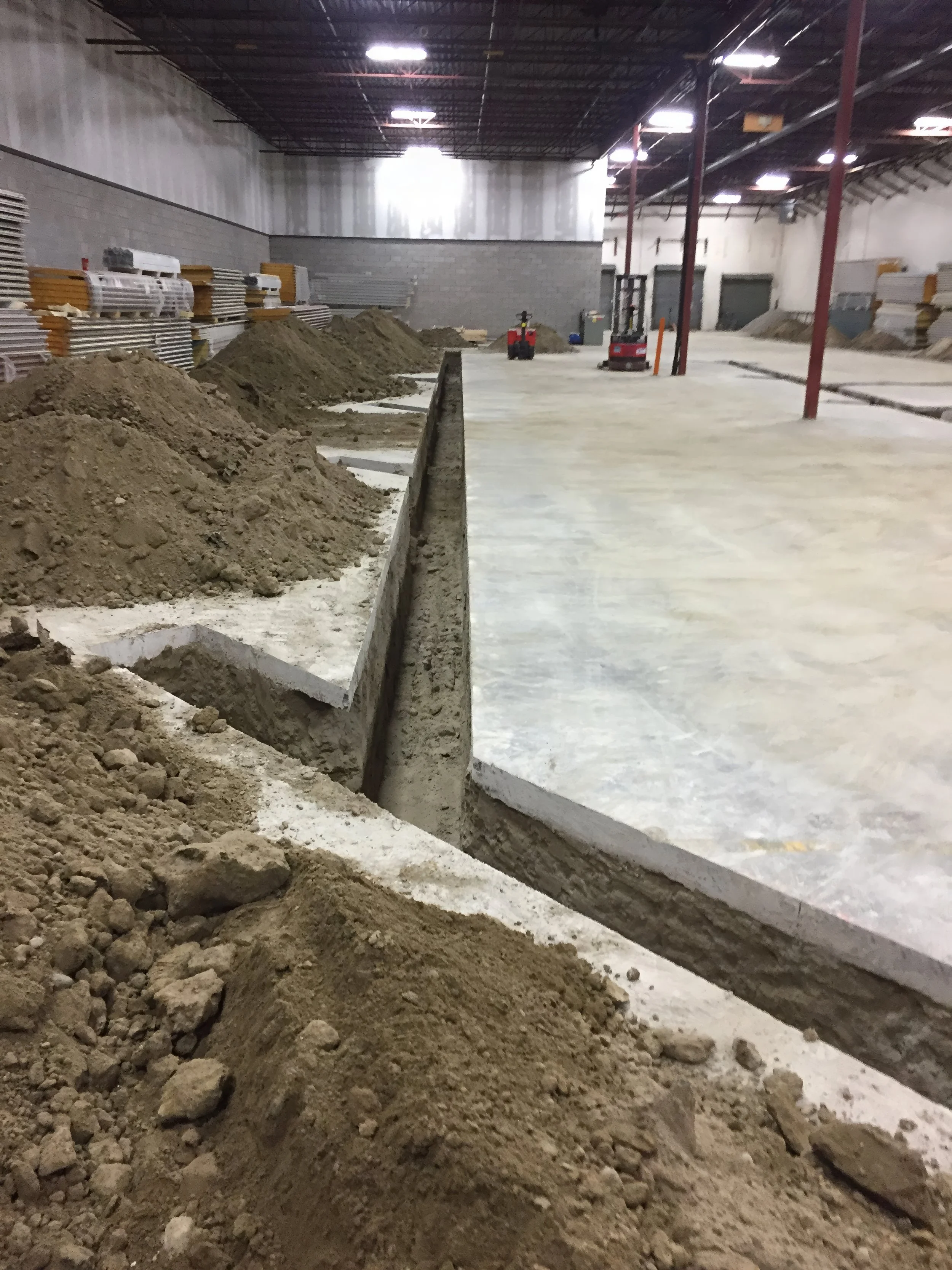 Large commercial warehouse renovation showing concrete slab cutting, deep trench excavation, and foundation work for infrastructure upgrades in Toronto