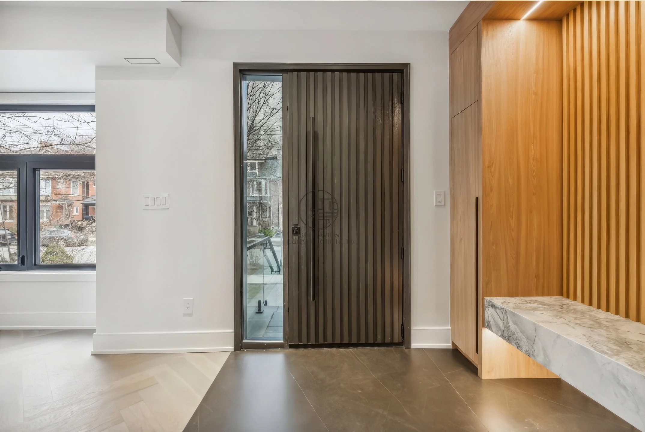 Contemporary entryway with wood slat accent wall, built-in bench with stone seat, glass door, and minimalist modern interior design.