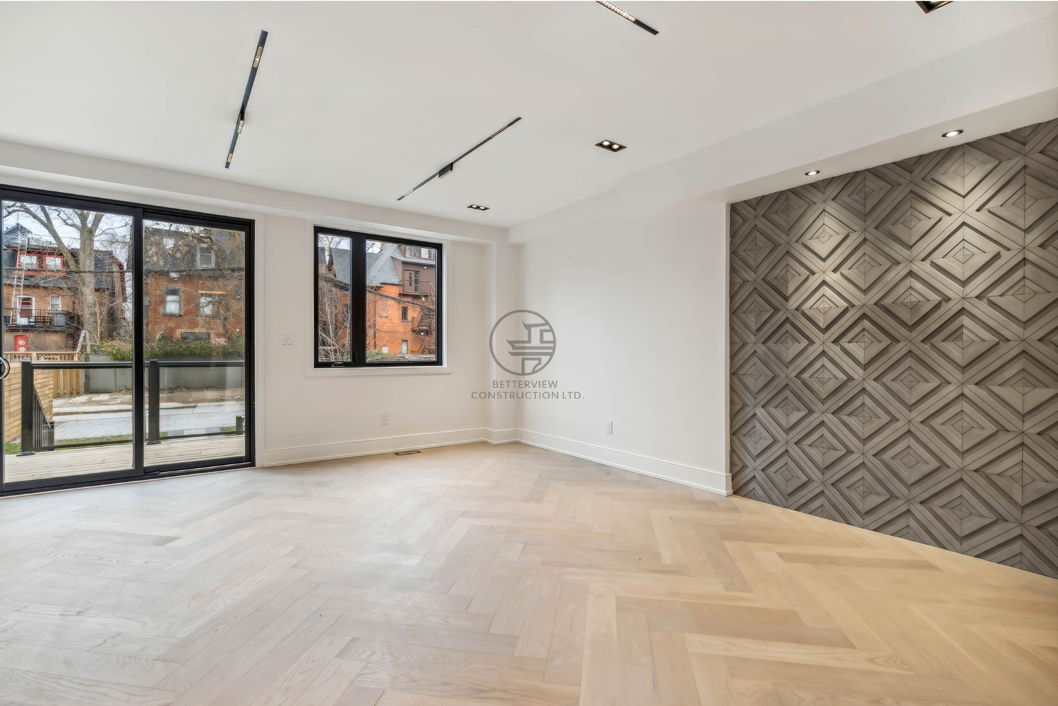 Modern living room with herringbone wood flooring, geometric feature wall, large windows, and sliding glass doors in a bright open space.