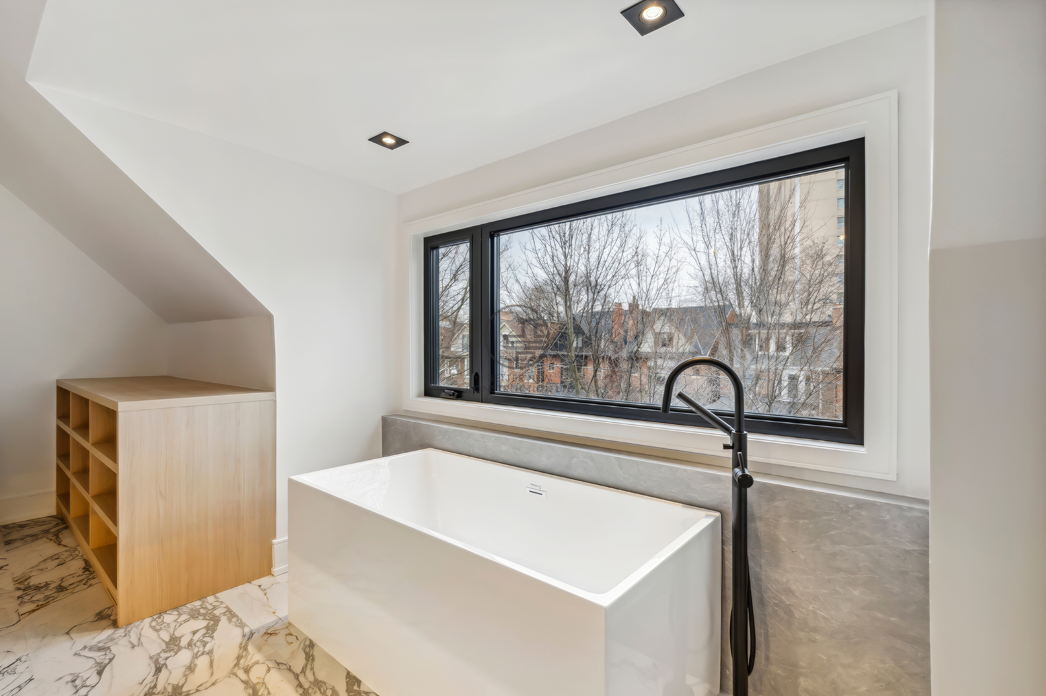 Modern bathroom with freestanding bathtub, large window view, marble flooring, and matte black floor-mounted faucet in a luxury home renovation project