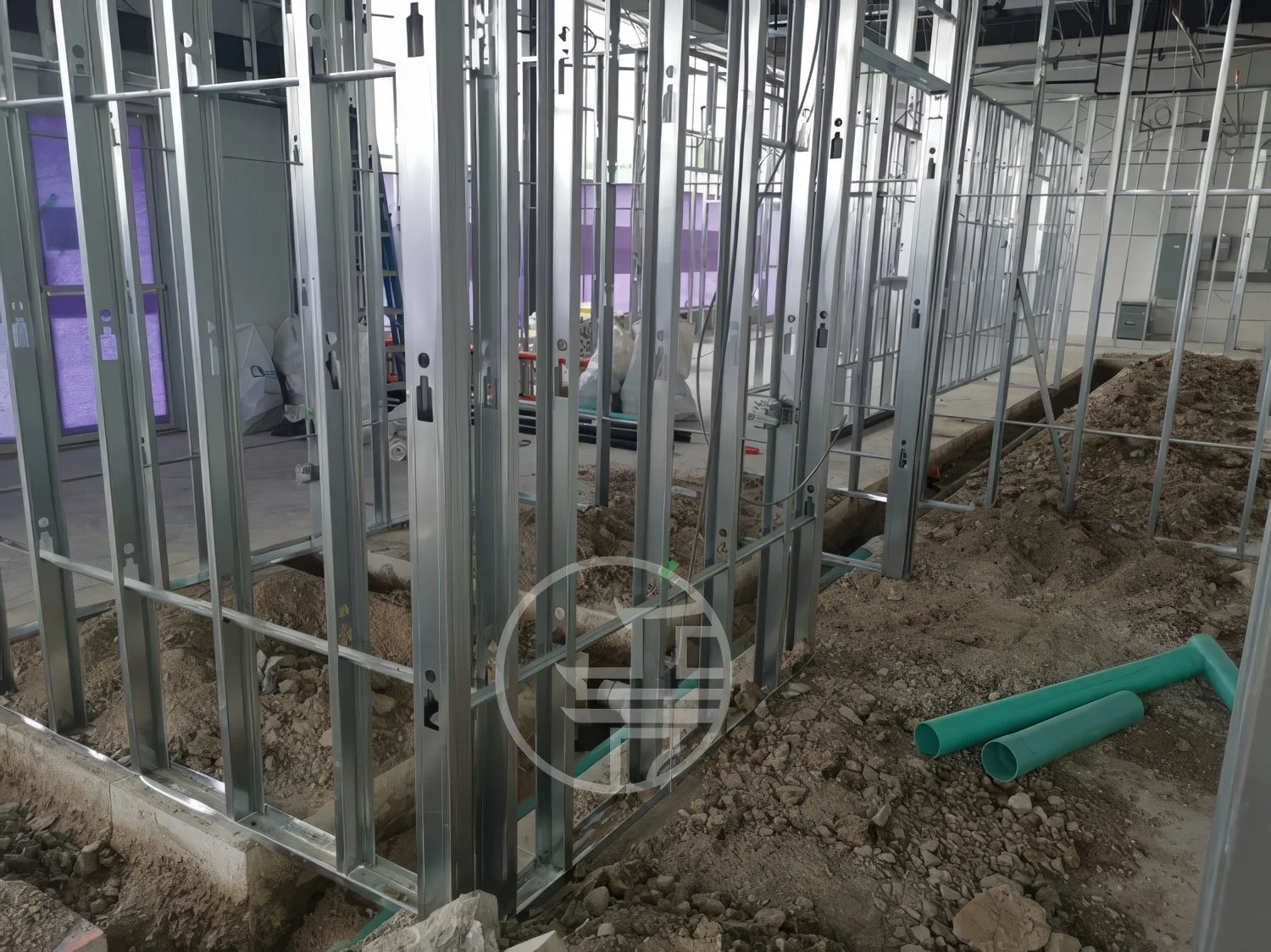 Commercial renovation showing plumbing rough-in with trenching, drainage pipes installation, and steel framing during interior construction