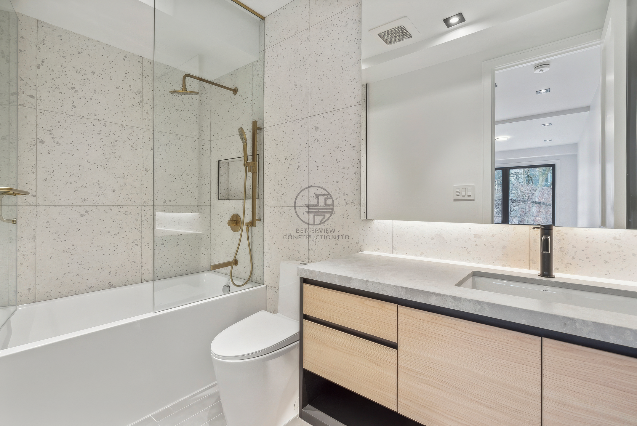 Modern bathroom renovation featuring a floating wood vanity, integrated sink, bathtub with glass shower enclosure, and gold fixtures with minimalist design.
