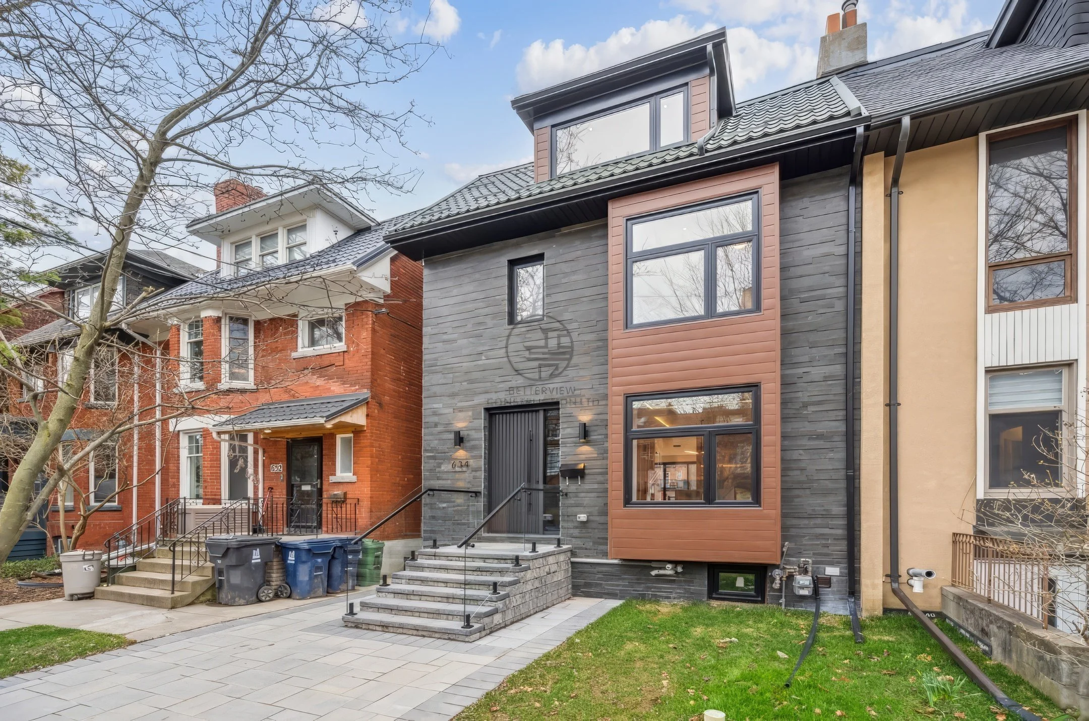 Modern home exterior renovation with mixed brick, stone, and wood facade, front steps with glass railing, and updated contemporary design.