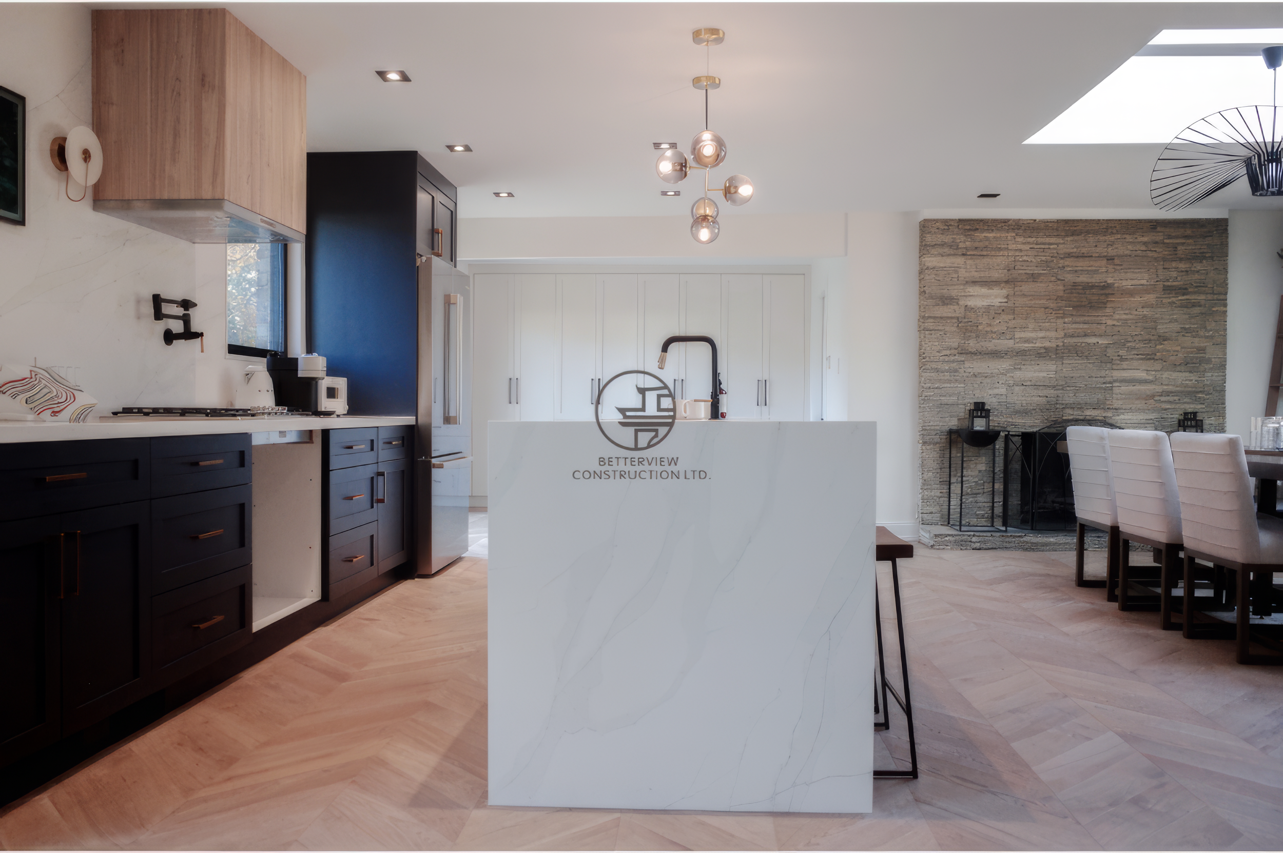 Modern kitchen renovation with a white waterfall island, custom cabinetry, and herringbone hardwood flooring.