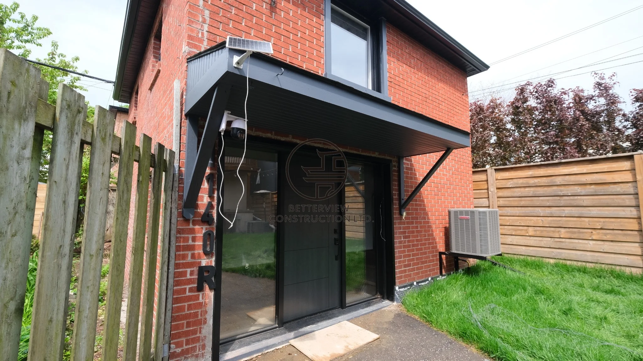 Rear patio entrance with sliding glass doors, black metal awning, brick exterior, and modern backyard access design.