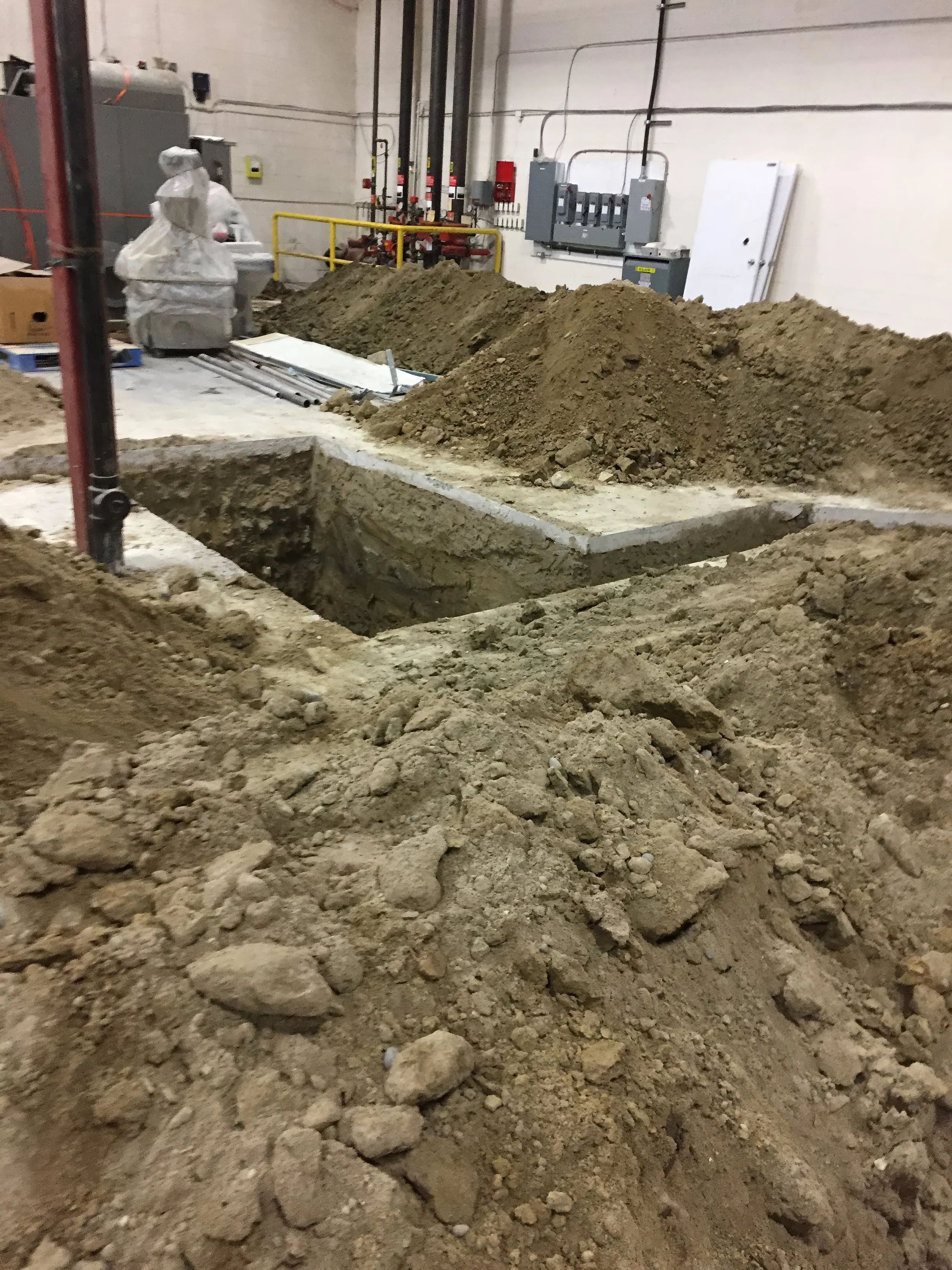 Commercial renovation showing trench excavation for plumbing and utility installation with exposed pipes and foundation work in a warehouse in Toronto