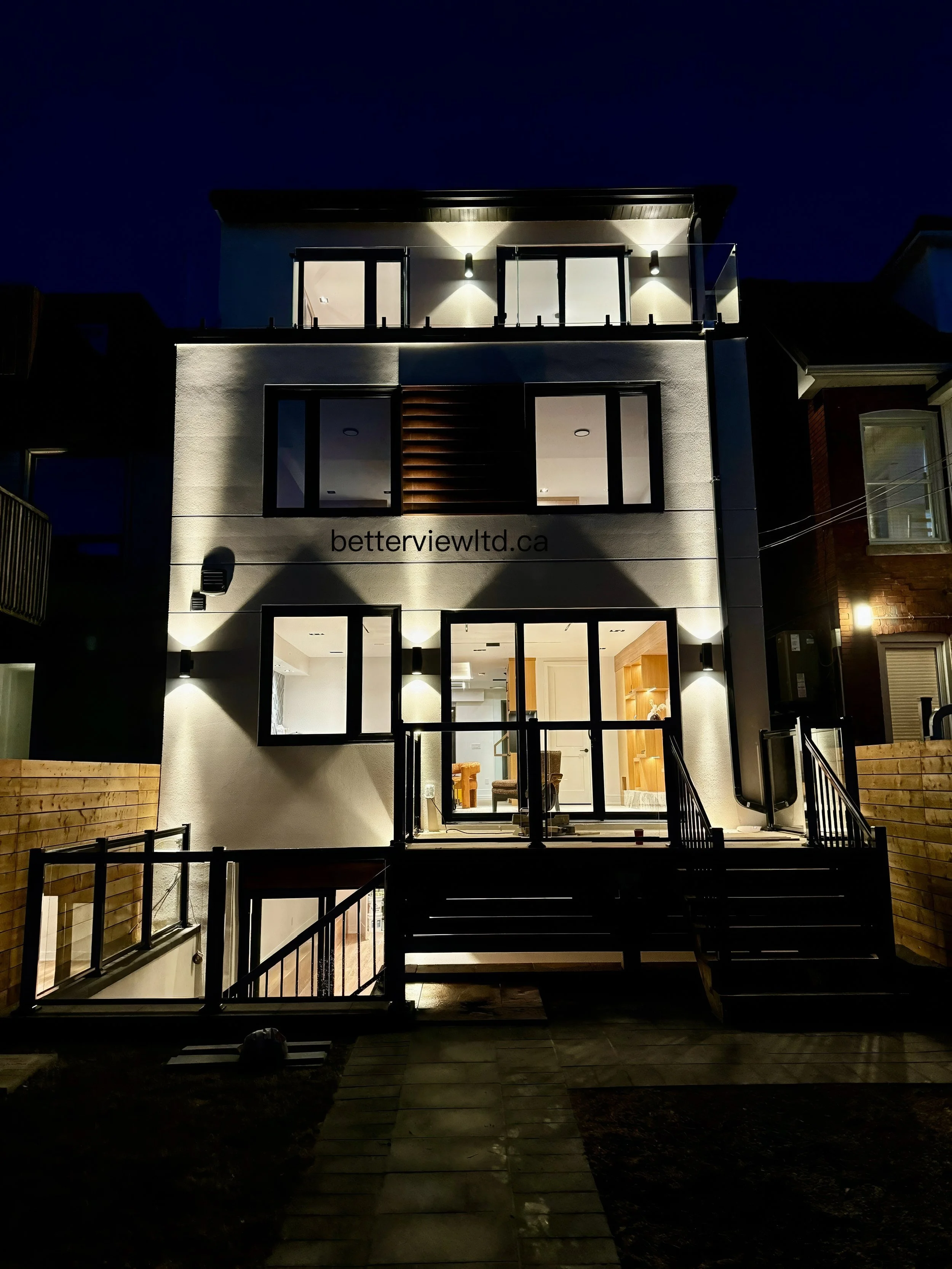 Contemporary custom home exterior at night with modern lighting, large windows, front steps, and sleek architectural design.