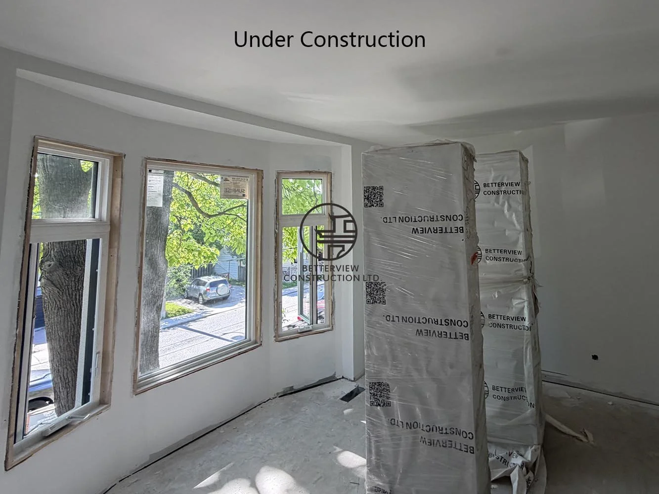 Bright living area under construction featuring large windows, drywall finishing, and an open concept layout in the rear addition.