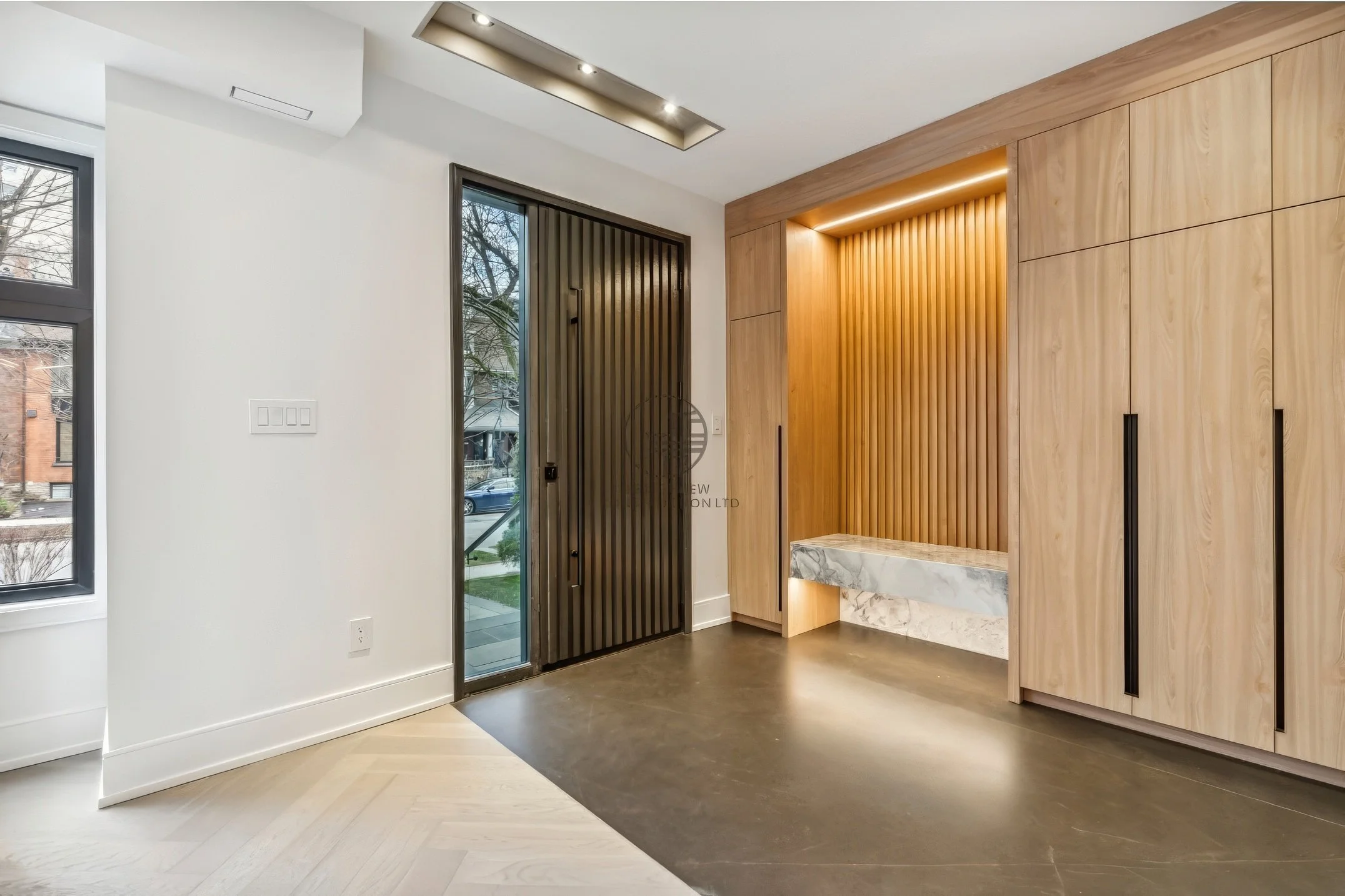 Modern entryway with built-in wood closet, vertical slat accent wall, integrated bench with lighting, and glass door in minimalist home design.
