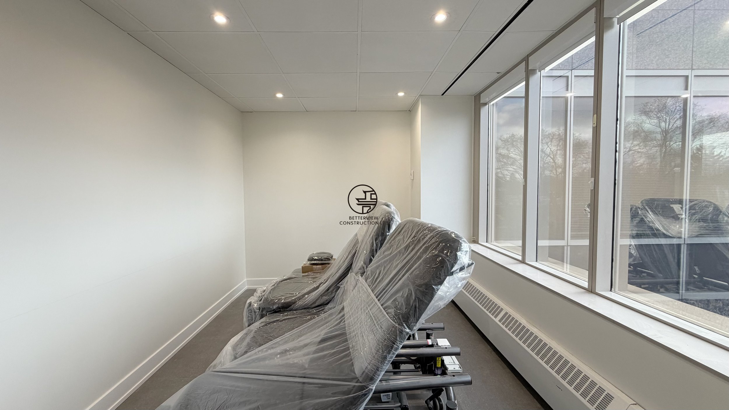Modern office room with large windows, natural light, and chairs setup in commercial renovation
