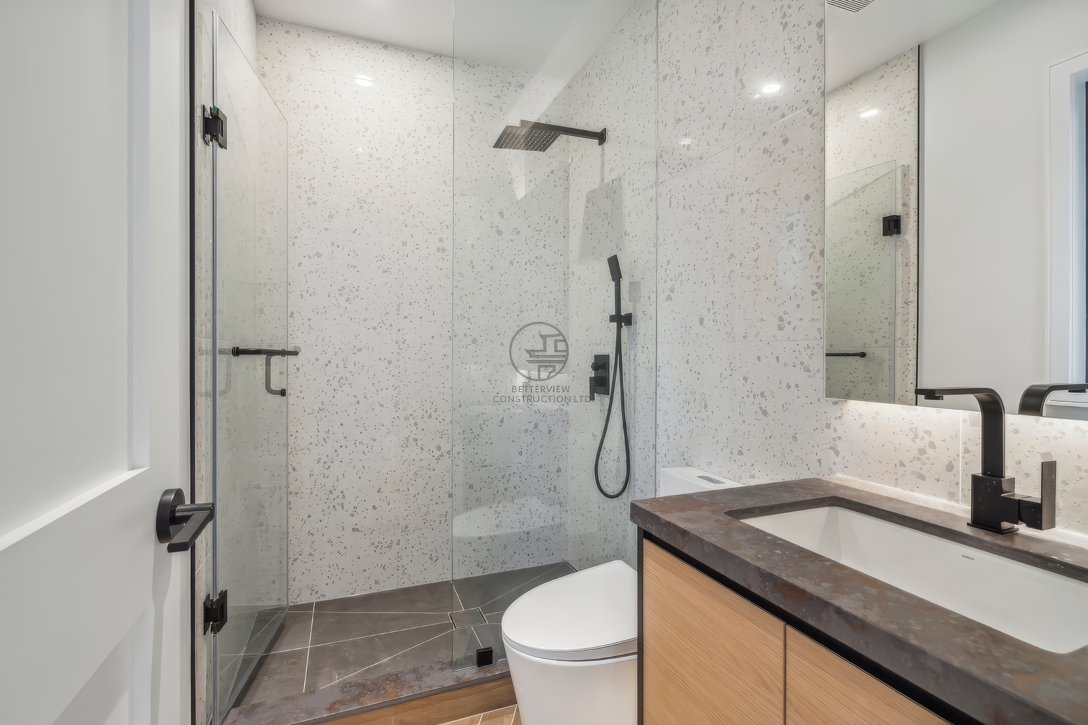 Modern bathroom with glass walk-in shower, speckled tile walls, floating vanity, and matte black fixtures in a residential home renovation project