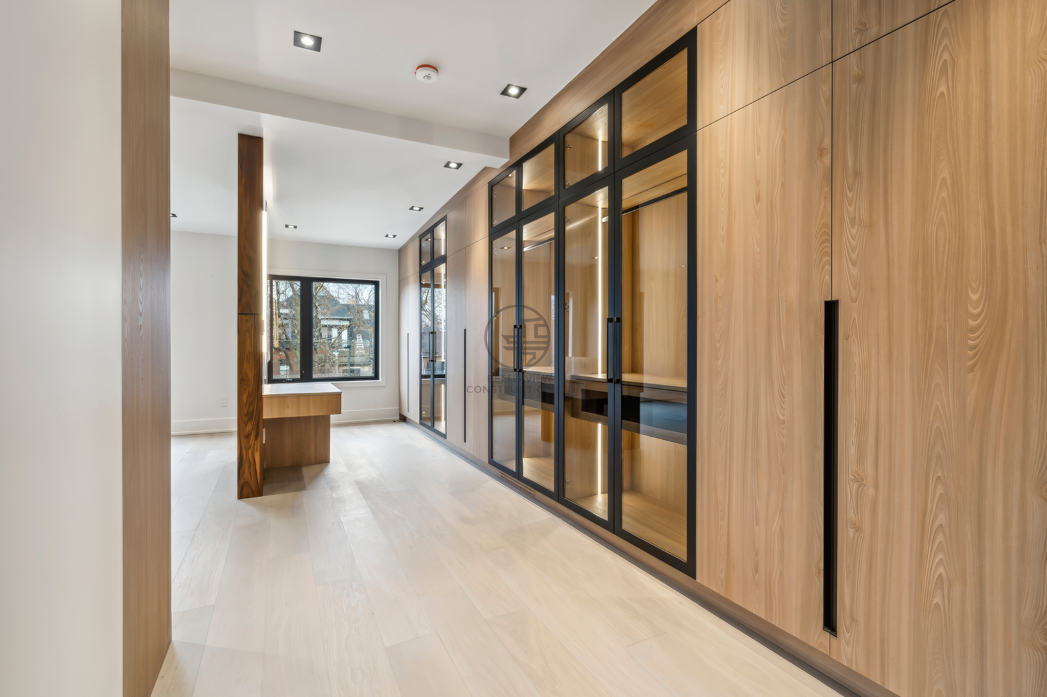 Modern interior hallway with custom wood cabinetry, glass partition closet, recessed lighting, and open-concept layout in a luxury home renovation project