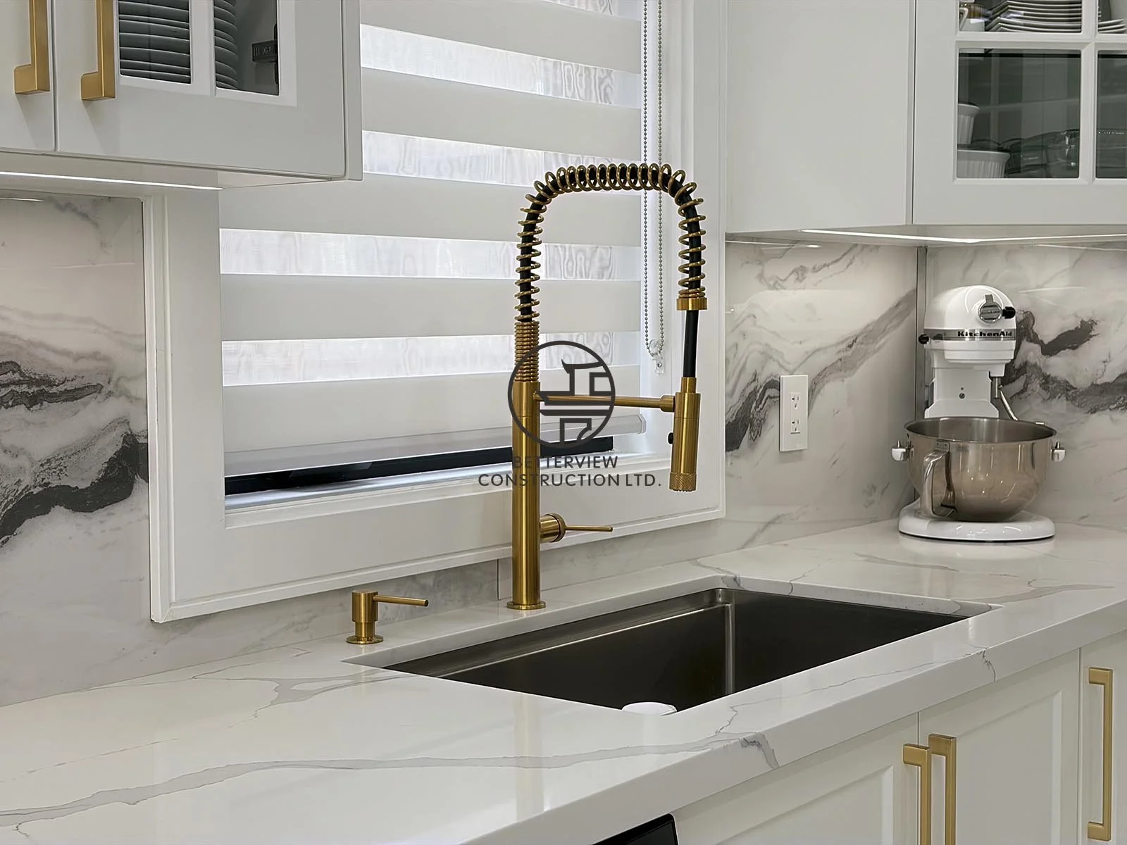 A brushed gold pull-down faucet, undermount sink, quartz countertops, and full-height backsplash create a functional and elegant kitchen workspace.