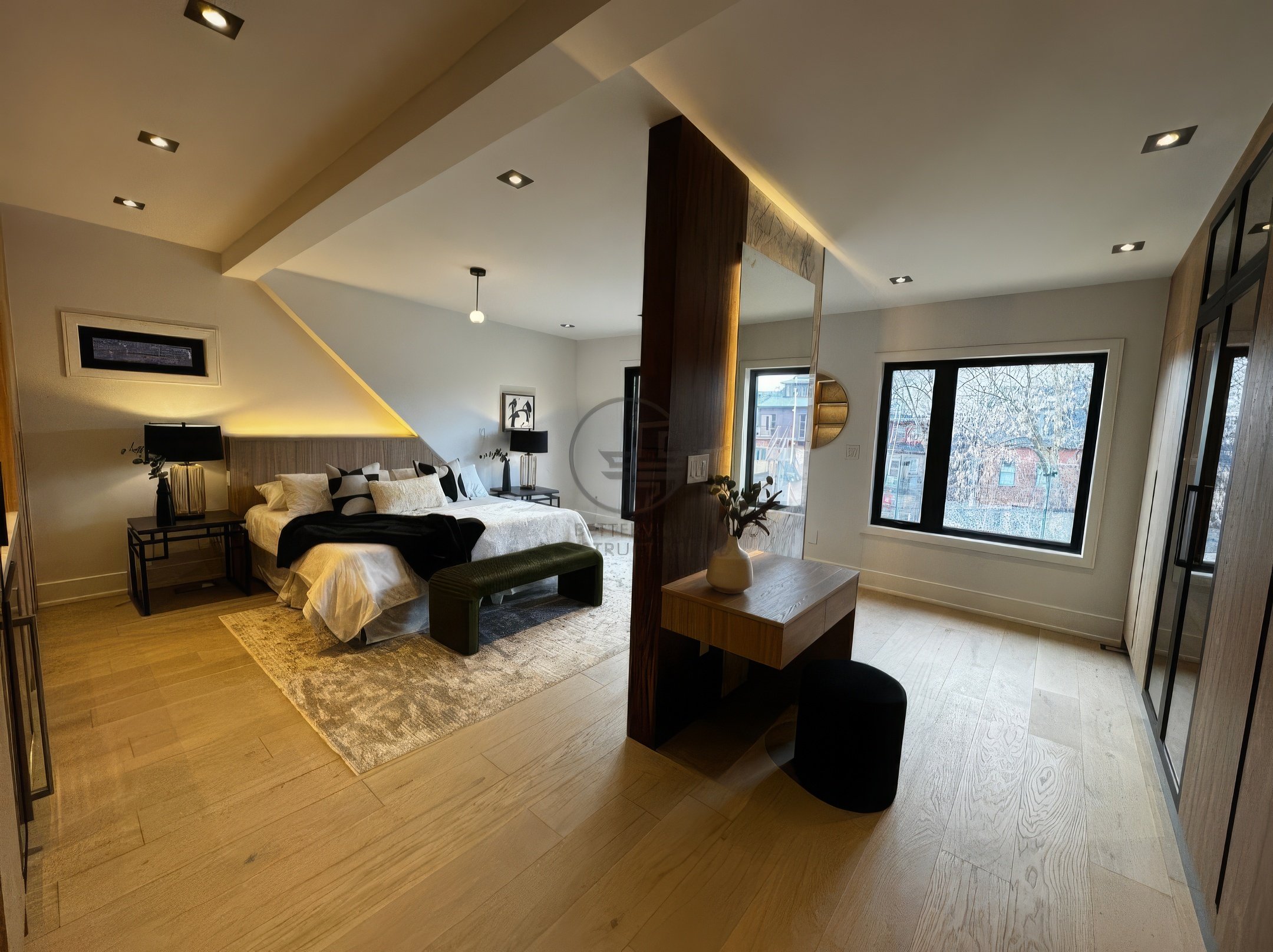Spacious modern bedroom with open layout, wood flooring, central partition with floating desk, large windows, and warm ambient lighting.