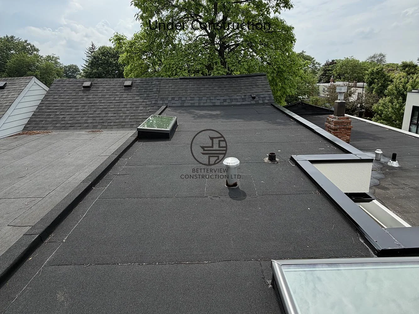 Completed flat roof system featuring roofing membrane, roof vents, and skylights installed above the rear addition.