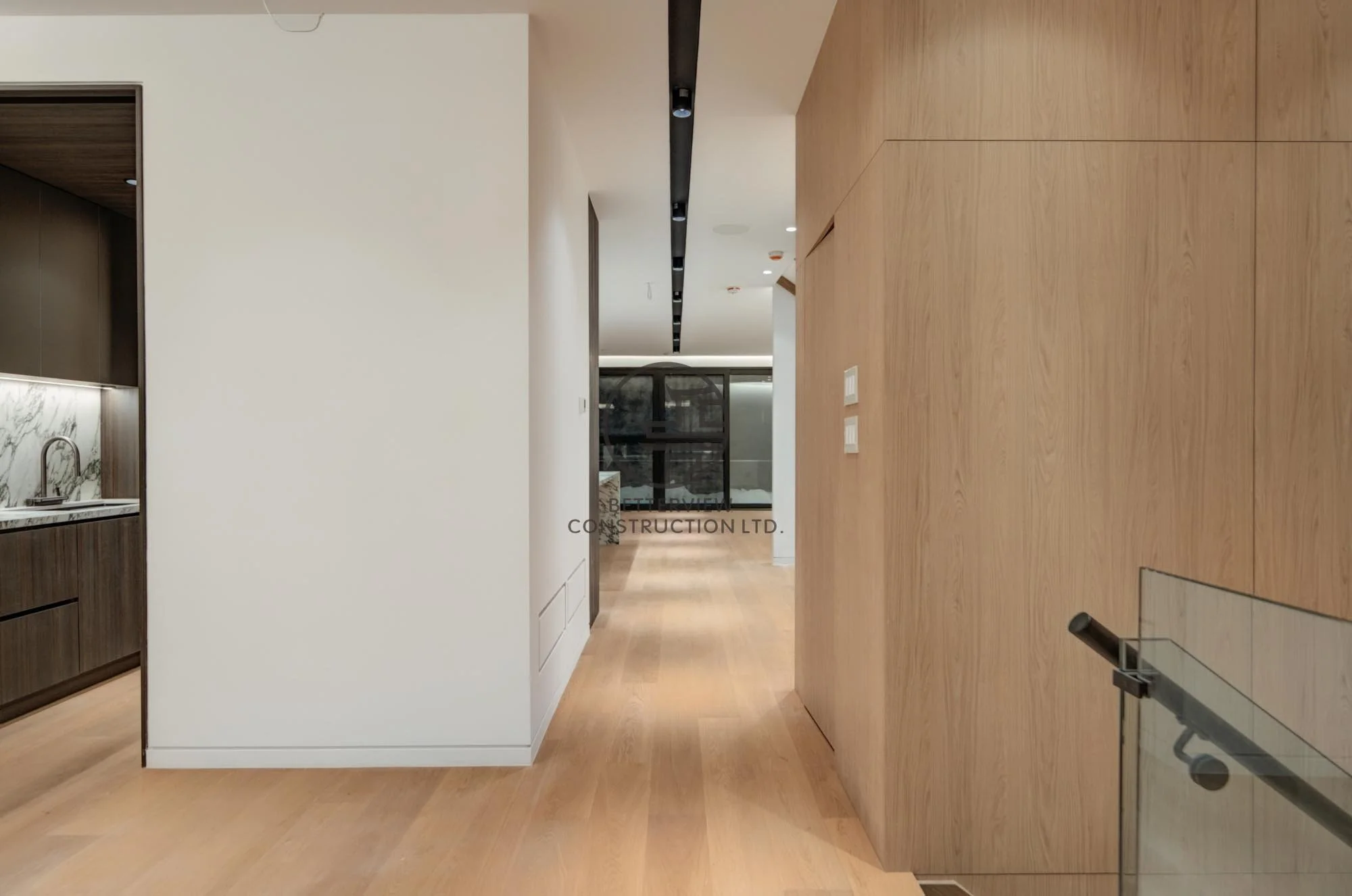 Modern home renovation featuring a minimalist hallway with open-concept layout, wood panel walls, light wood flooring, and seamless transition to kitchen space.